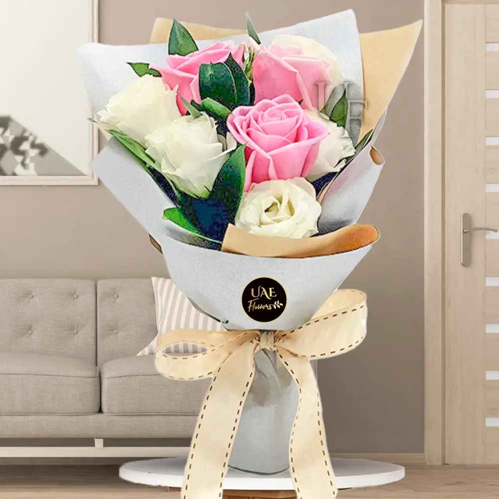 Bouquet of pink and white roses wrapped in elegant paper with a beige ribbon bow