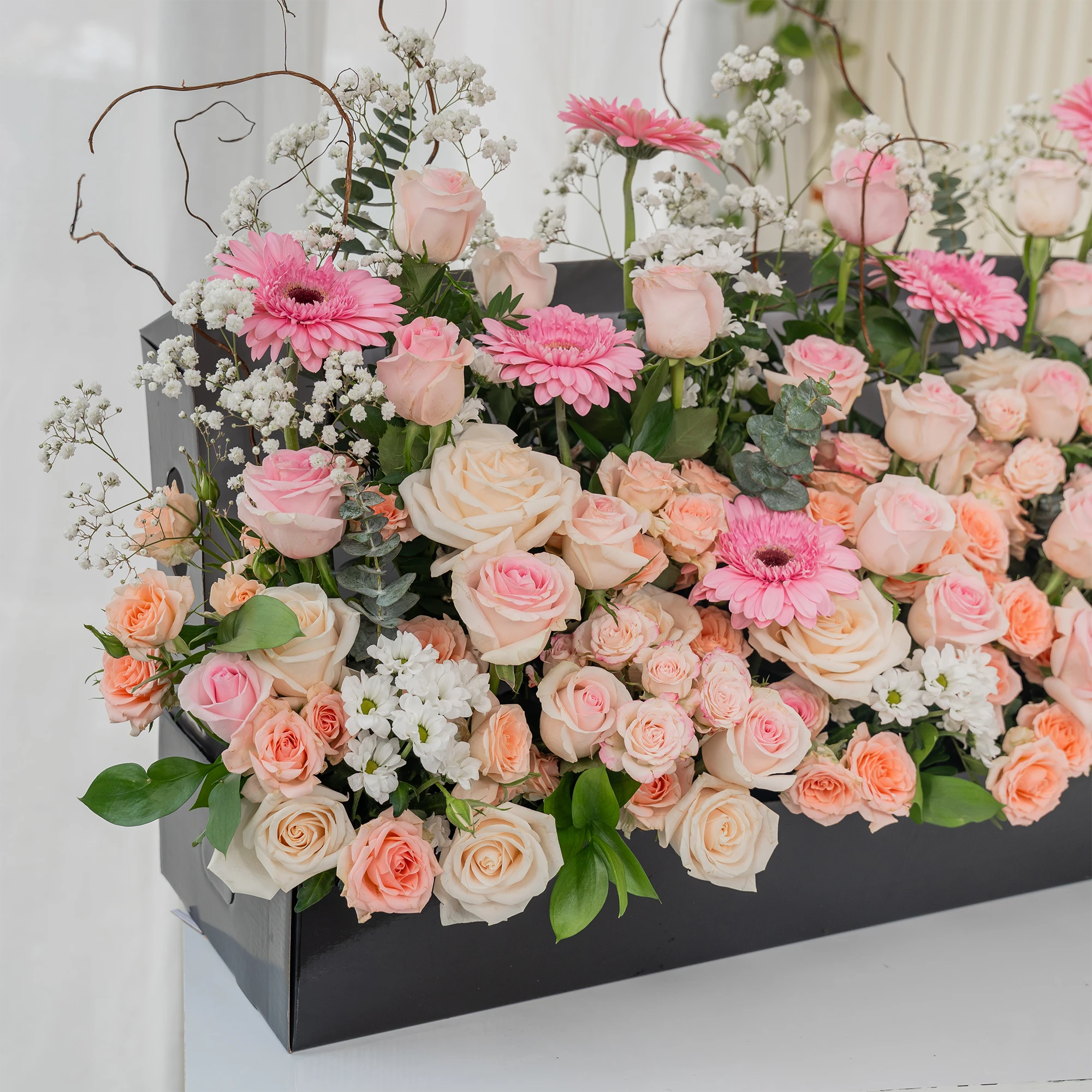 Arrangement of 8 pink gerberas, 30 pink roses, 10 peach roses, 10 Pink spray roses and 5 white chrysanthemums with green fillers and baby's breath in a long black box.