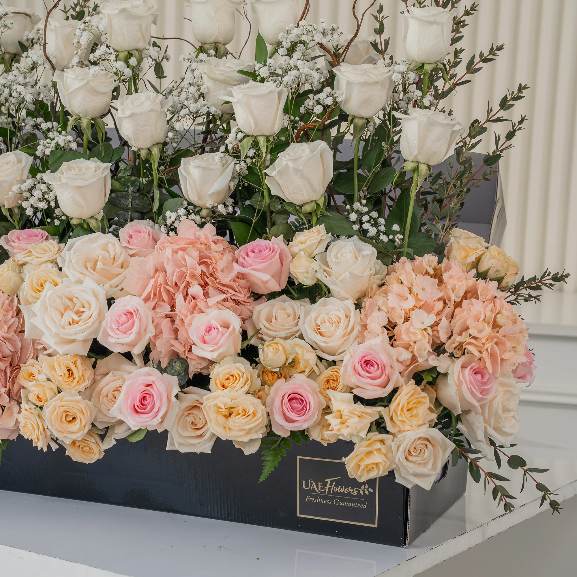 Arrangement of 30 White roses, 20 pink roses, 4 pink hydrangeas and 10 peach spray roses with green fillers and baby's breath in a long black box.