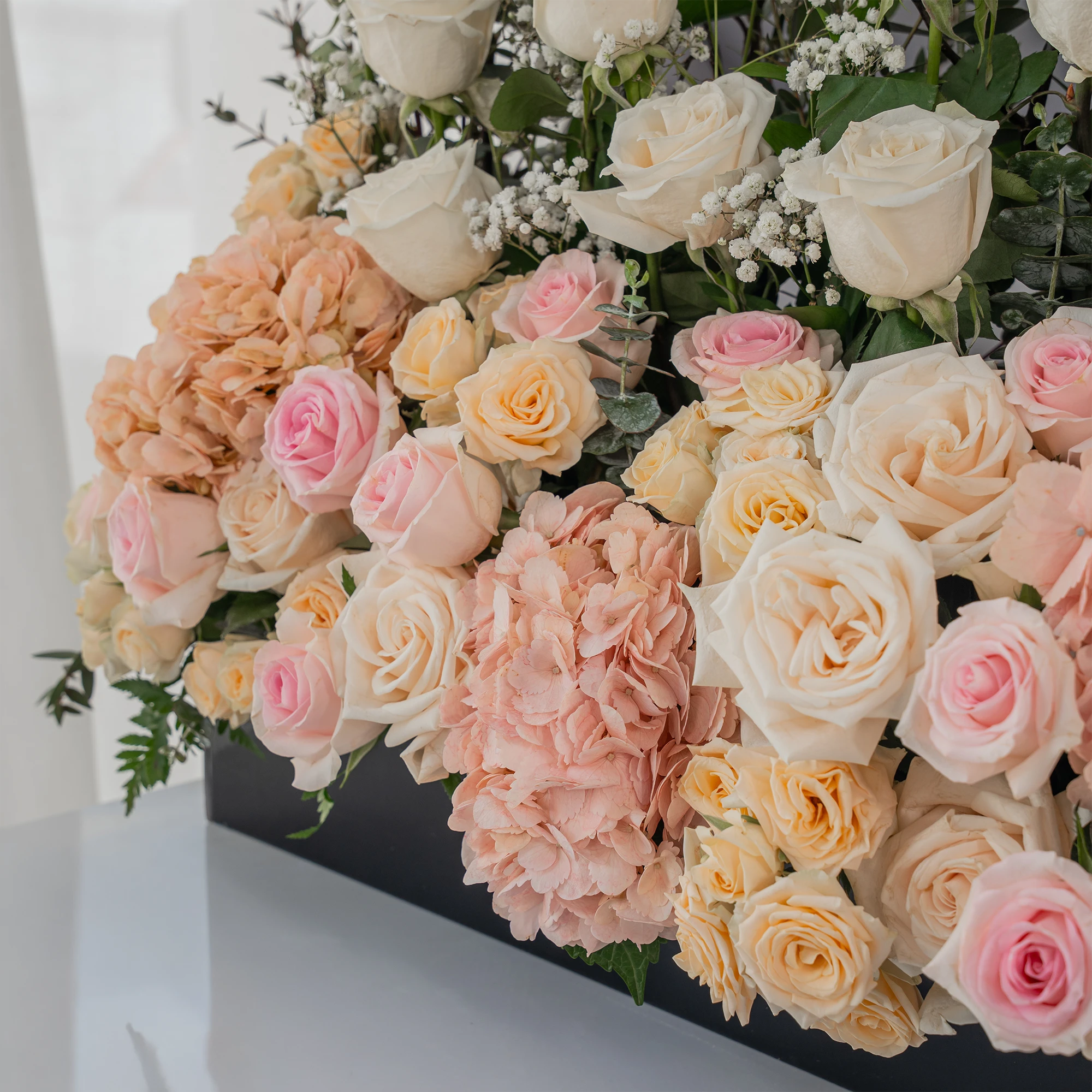 Arrangement of 30 White roses, 20 pink roses, 4 pink hydrangeas and 10 peach spray roses with green fillers and baby's breath in a long black box.