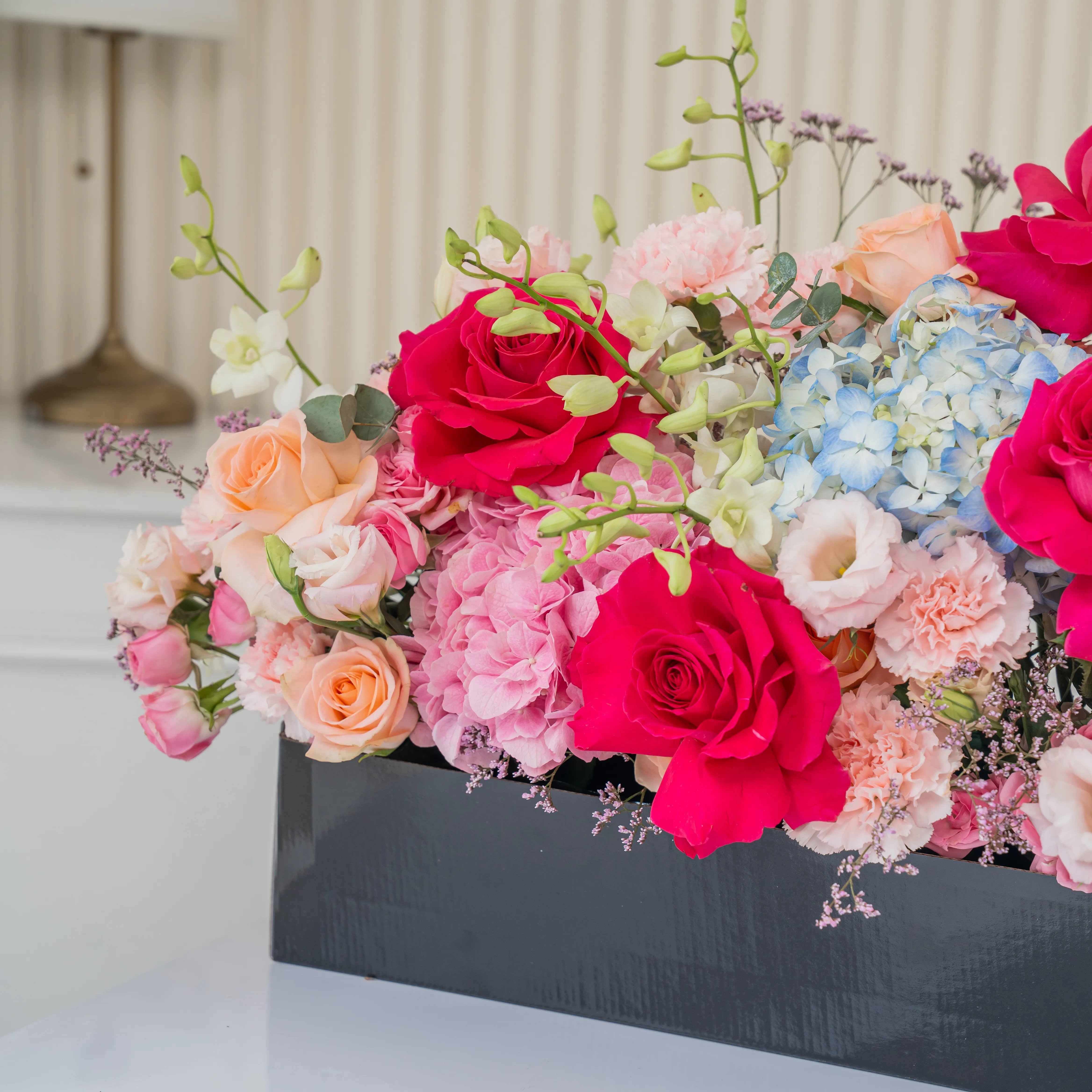 Arrangement of 4 blue hydrangeas, 2 pink hydrangeas, 20 pink carnations, 10 pink spray roses, 10 peach roses and 4 pink gerberas with green fillers in a long black box.