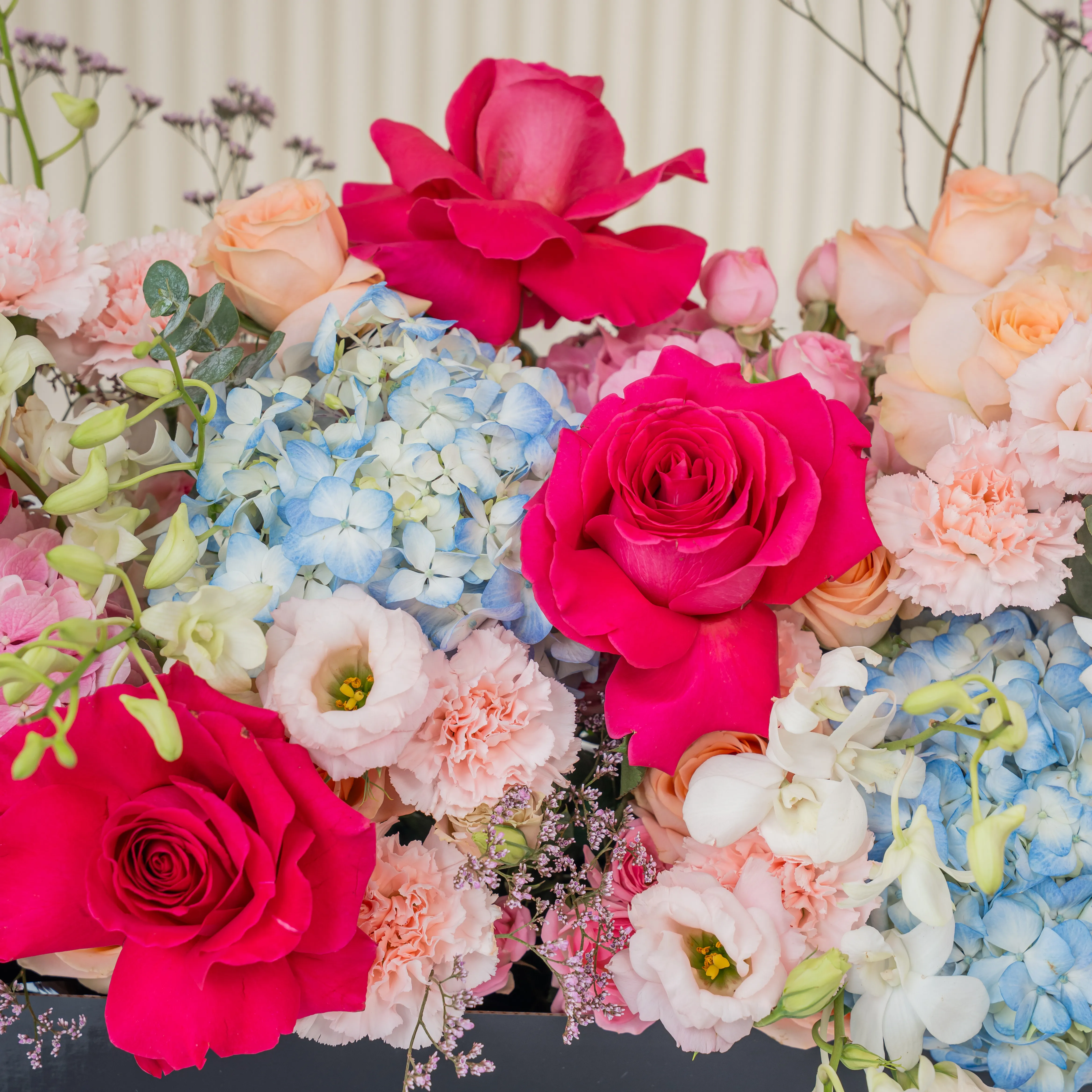 Arrangement of 4 blue hydrangeas, 2 pink hydrangeas, 20 pink carnations, 10 pink spray roses, 10 peach roses and 4 pink gerberas with green fillers in a long black box.