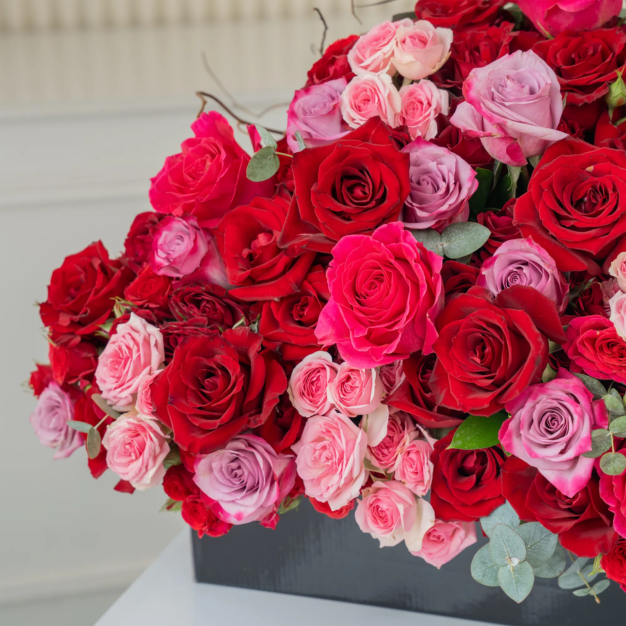 Arrangement of 20 red roses, 20 purple roses, 10 fuchsia roses, 20 red spray roses and 10 pink spray roses with green fillers in a long black box.