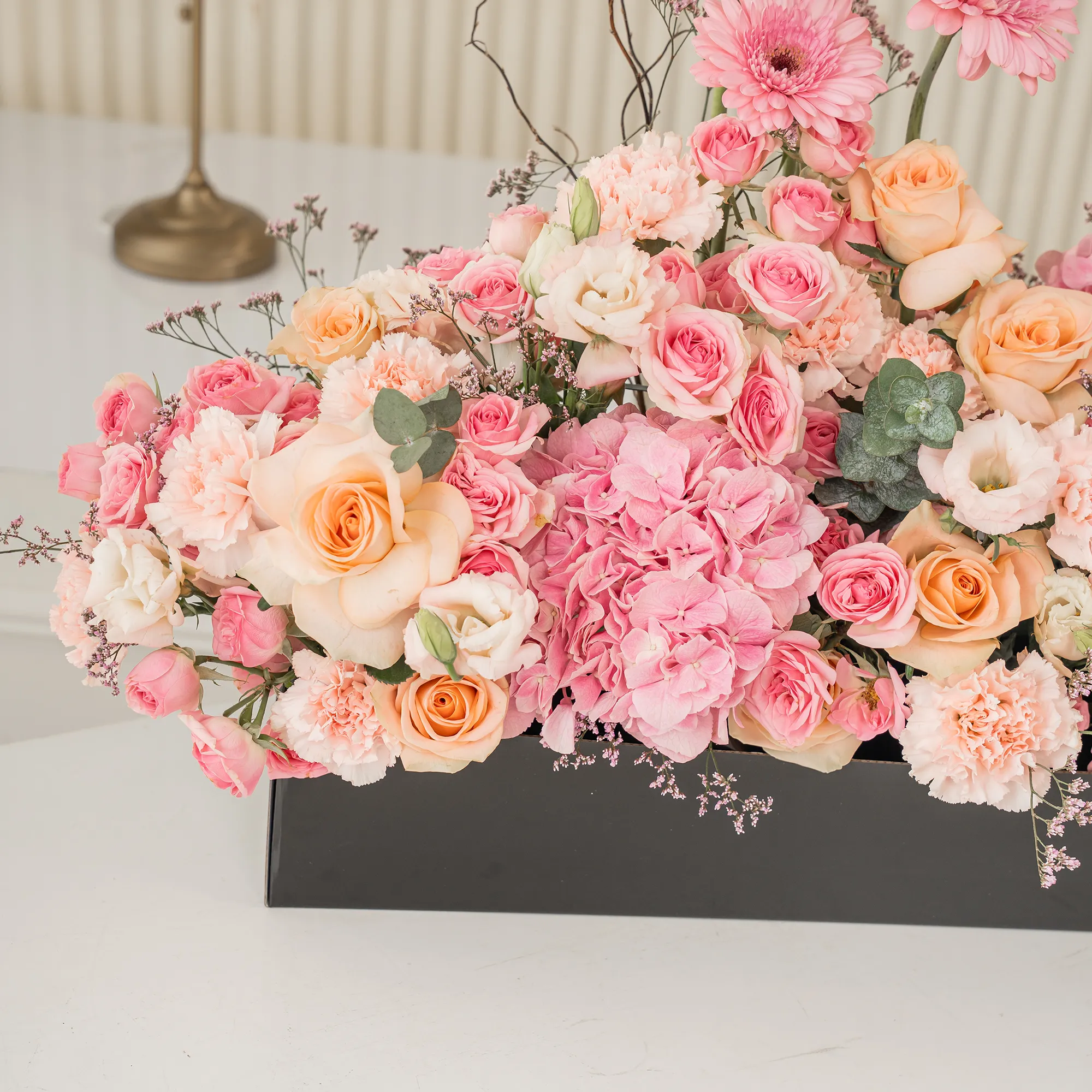 Arrangement of 4 pink gerberas, 3 pink hydrangeas, 20 pink carnations, 20 pink spray roses and 30 peach roses with green fillers in a long black box.