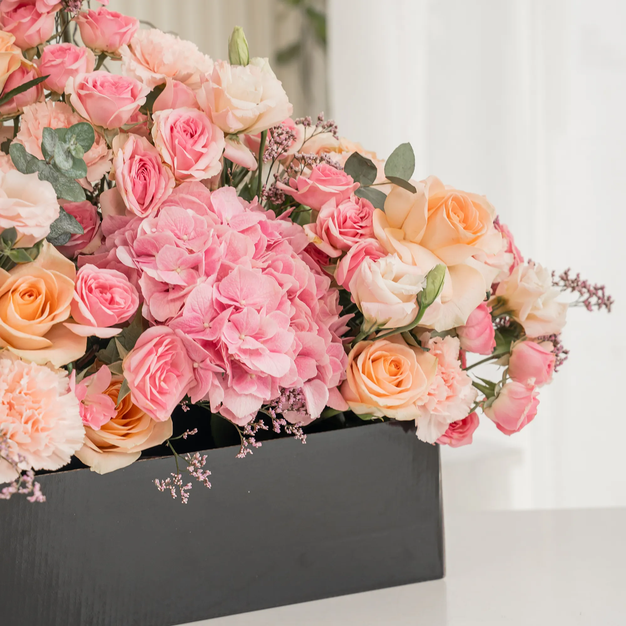 Arrangement of 4 pink gerberas, 3 pink hydrangeas, 20 pink carnations, 20 pink spray roses and 30 peach roses with green fillers in a long black box.