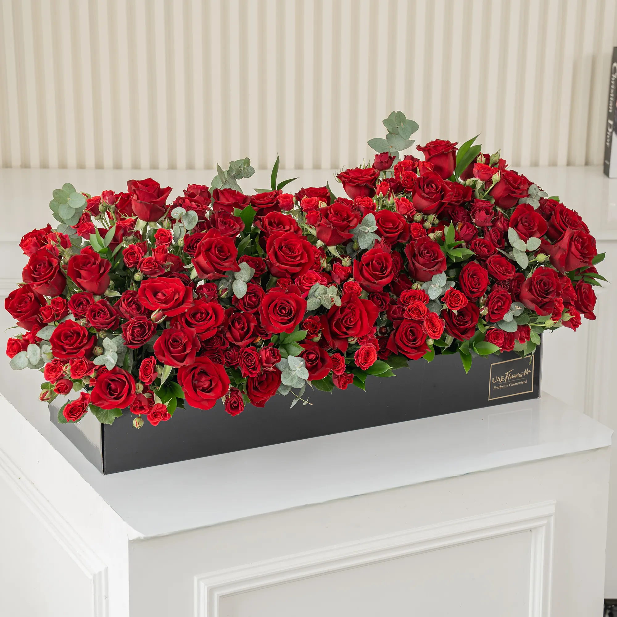 Arrangement of 50 red roses and 30 red spray roses with green fillers in a long black box.
