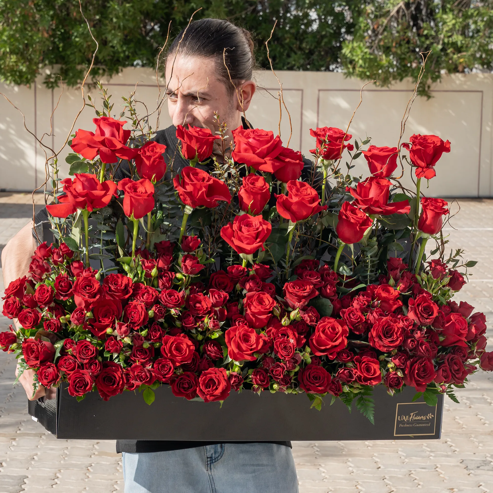 Arrangement of 50 red roses and 20 red spray roses with green fillers in a long black box.