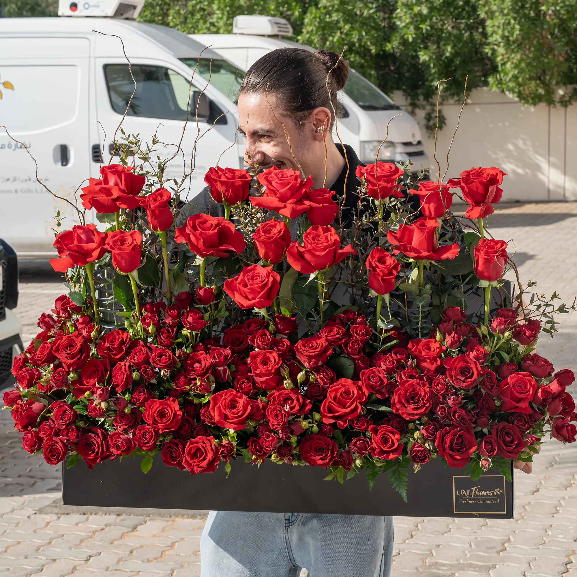 Arrangement of 50 red roses and 20 red spray roses with green fillers in a long black box.