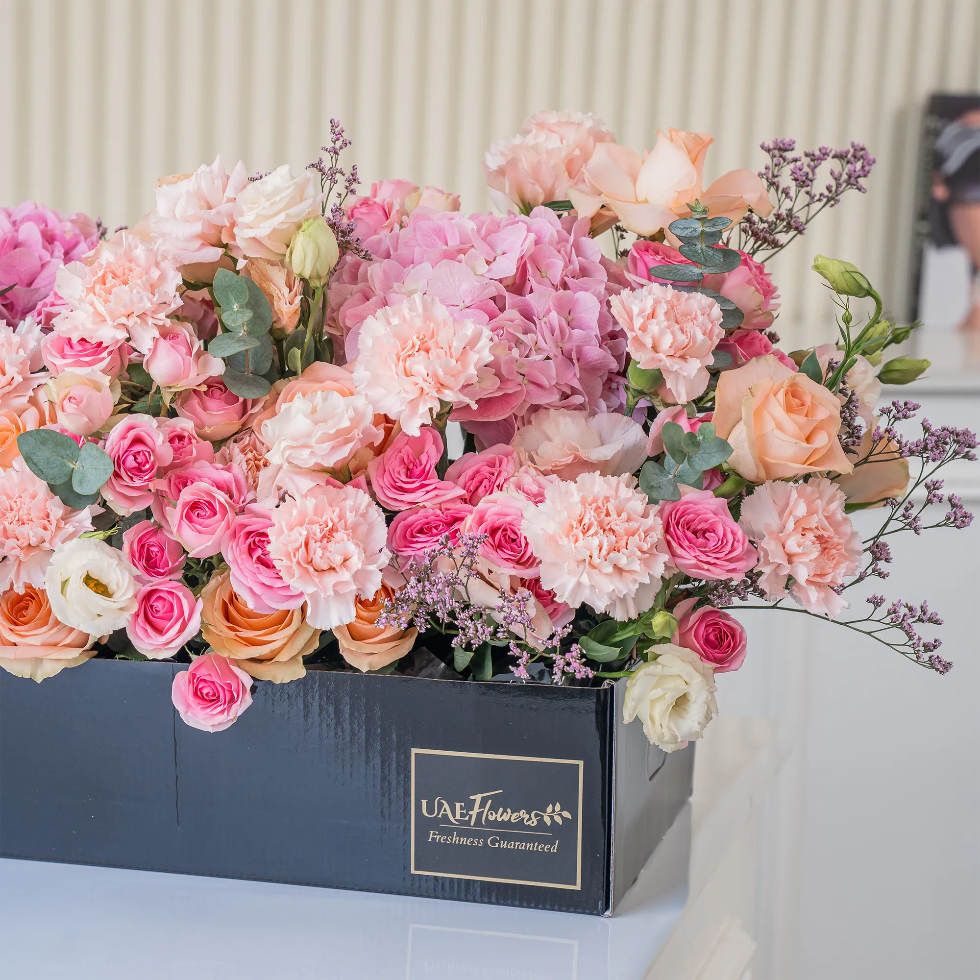 Arrangement of 20 peach roses, 20 pink carnations, 20 pink spray roses and 3 pink hydrangeas with green fillers in a long black box.