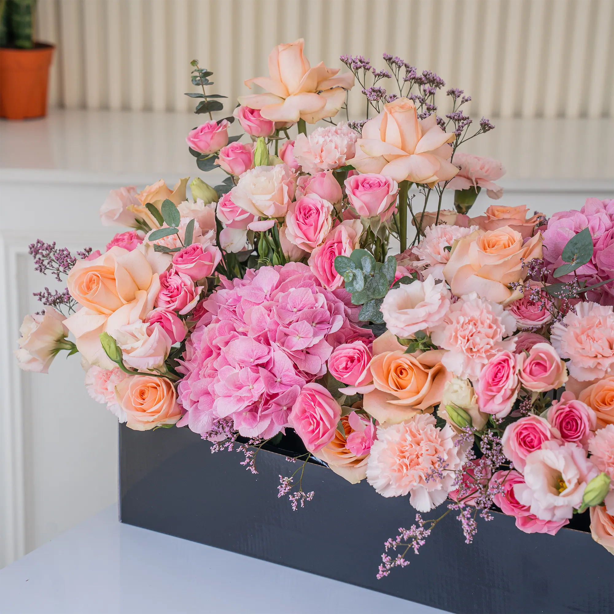 Arrangement of 20 peach roses, 20 pink carnations, 20 pink spray roses and 3 pink hydrangeas with green fillers in a long black box.