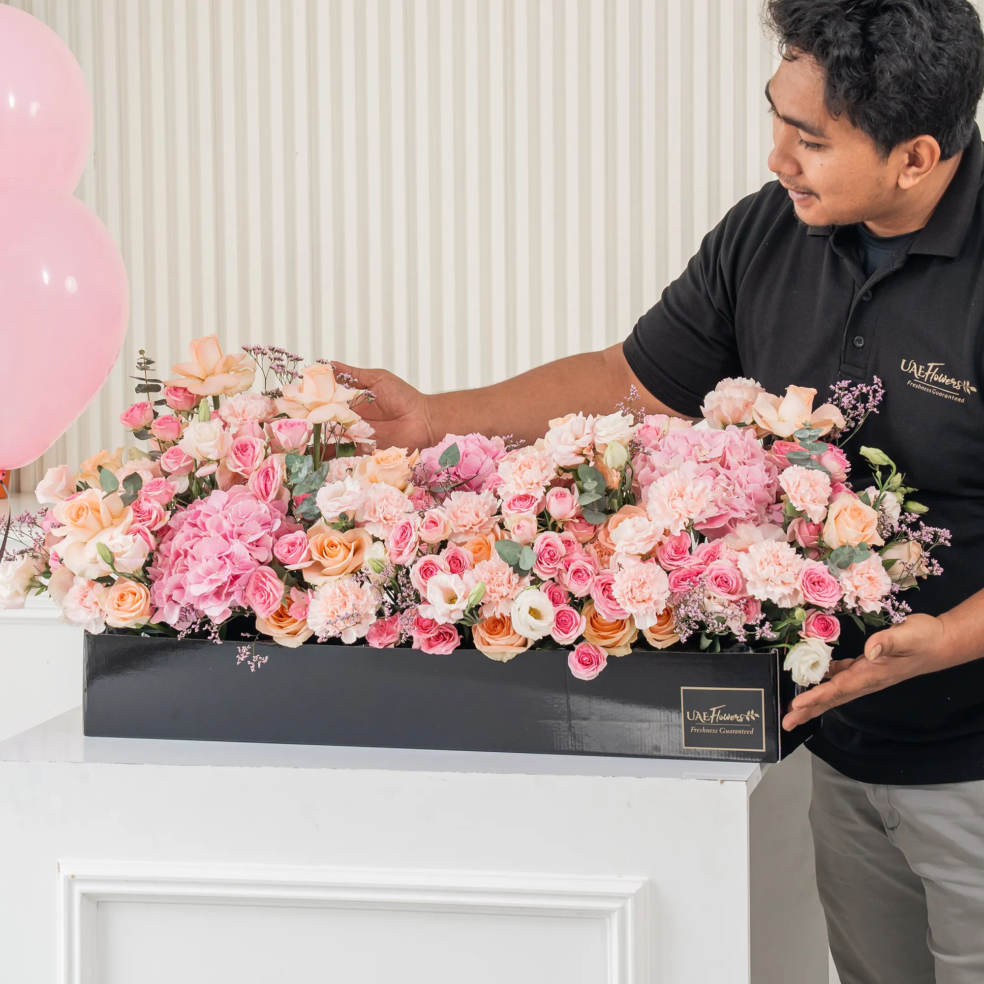 Arrangement of 20 peach roses, 20 pink carnations, 20 pink spray roses and 3 pink hydrangeas with green fillers in a long black box.