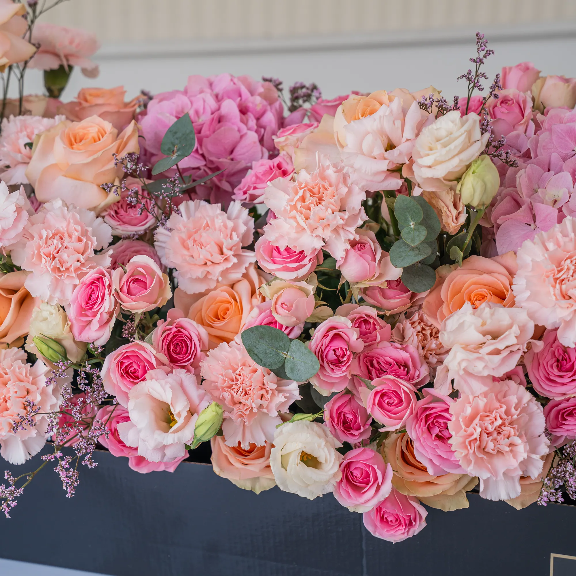 Arrangement of 20 peach roses, 20 pink carnations, 20 pink spray roses and 3 pink hydrangeas with green fillers in a long black box.
