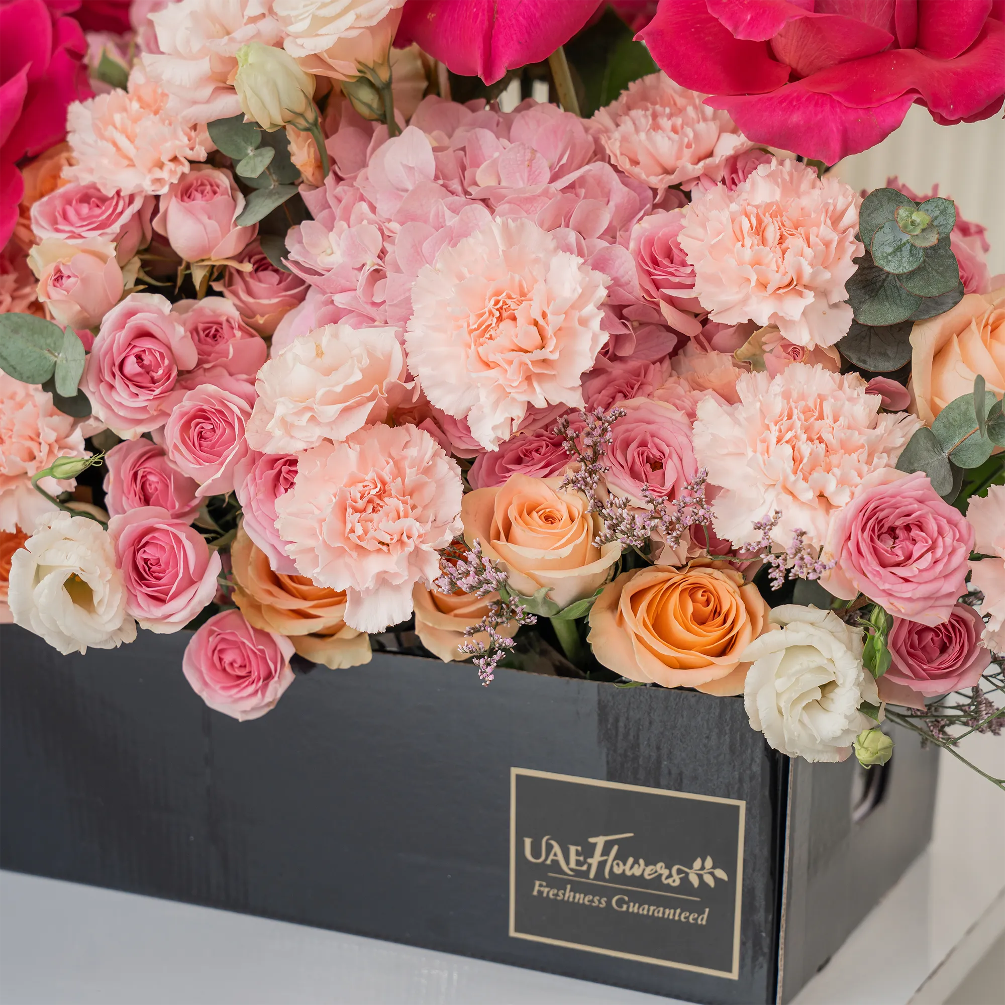 Arrangement of 10 fuchsia roses, 20 pink carnations, 20 pink spray roses, 20 peach roses and 2 pink hydrangeas with green fillers in a long black box.