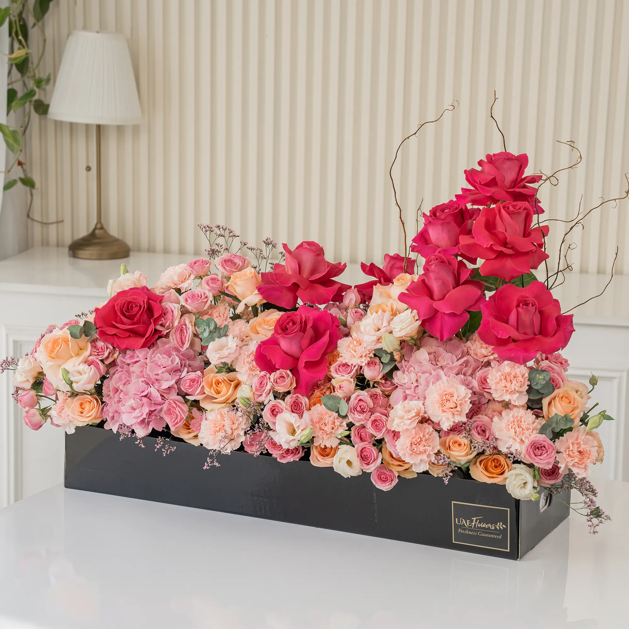 Arrangement of 10 fuchsia roses, 20 pink carnations, 20 pink spray roses, 20 peach roses and 2 pink hydrangeas with green fillers in a long black box.