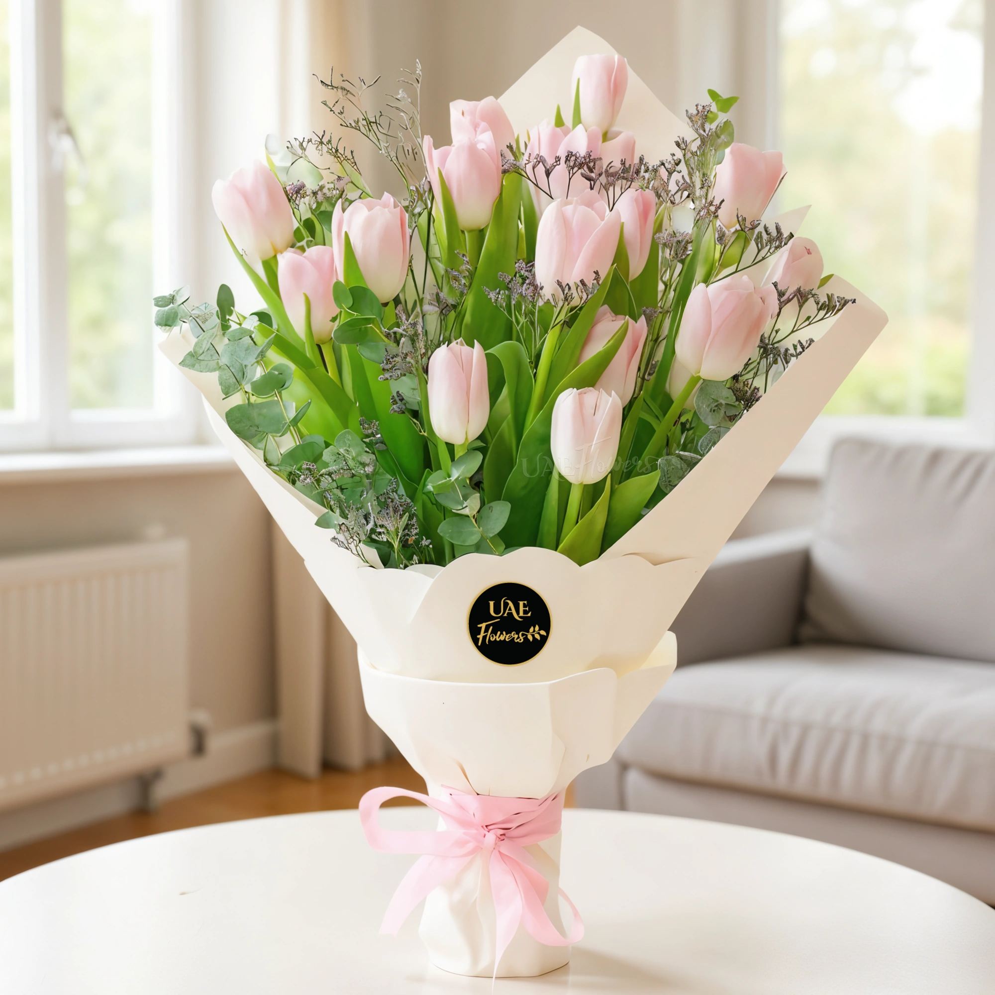 A bouquet of 15 pink tulips with greens in white wrapping paper tied with pink ribbon