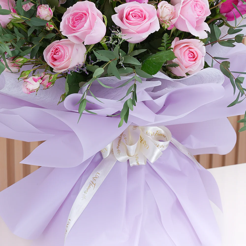 A bouquet of 10 pink roses, 10 purple roses and 3 pink spray roses with eucalyptus leaf and limonium fillers in pink wrapping paper tied with pink ribbon