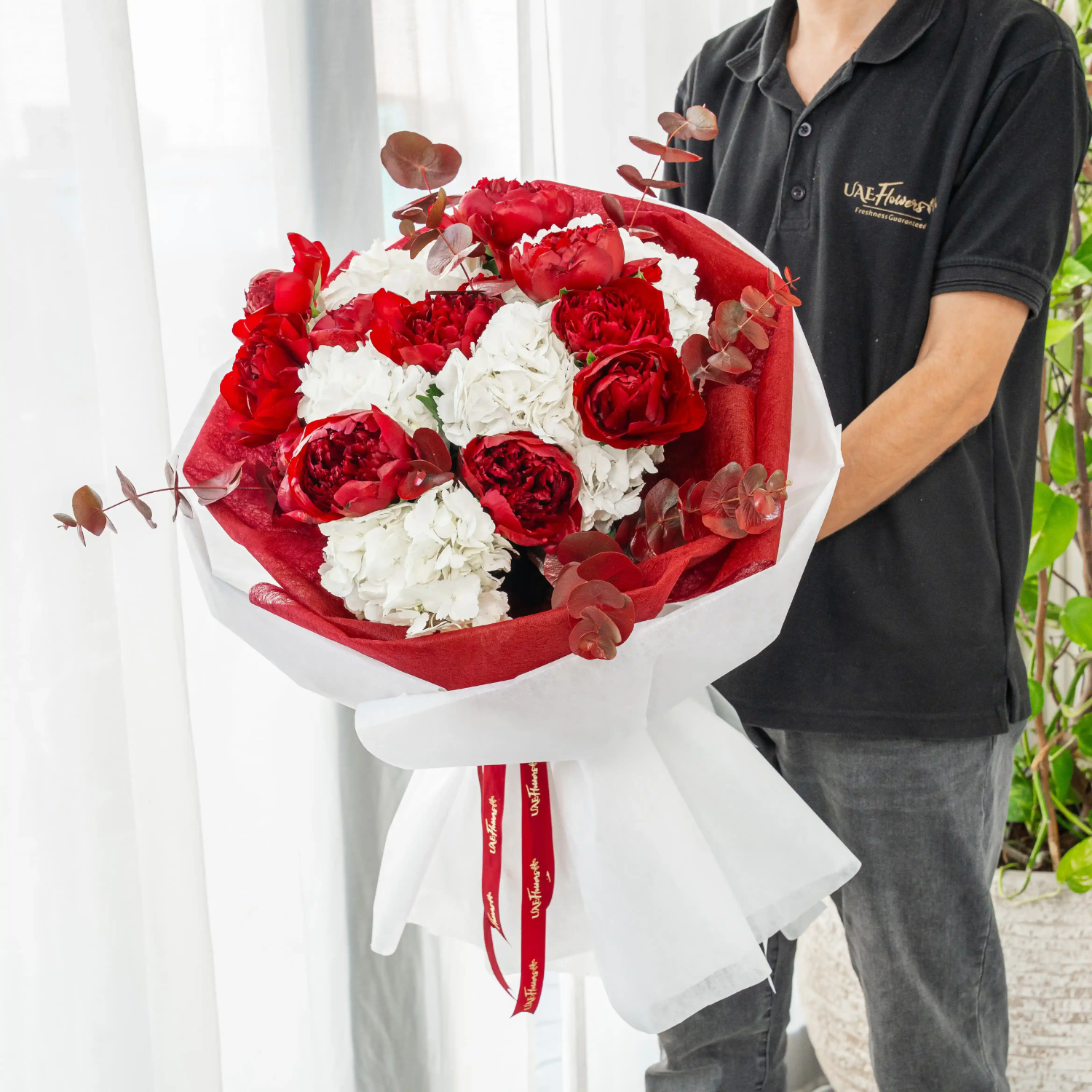 Festive bouquet with red peonies, white hydrangeas, and eucalyptus in red and white wrapping