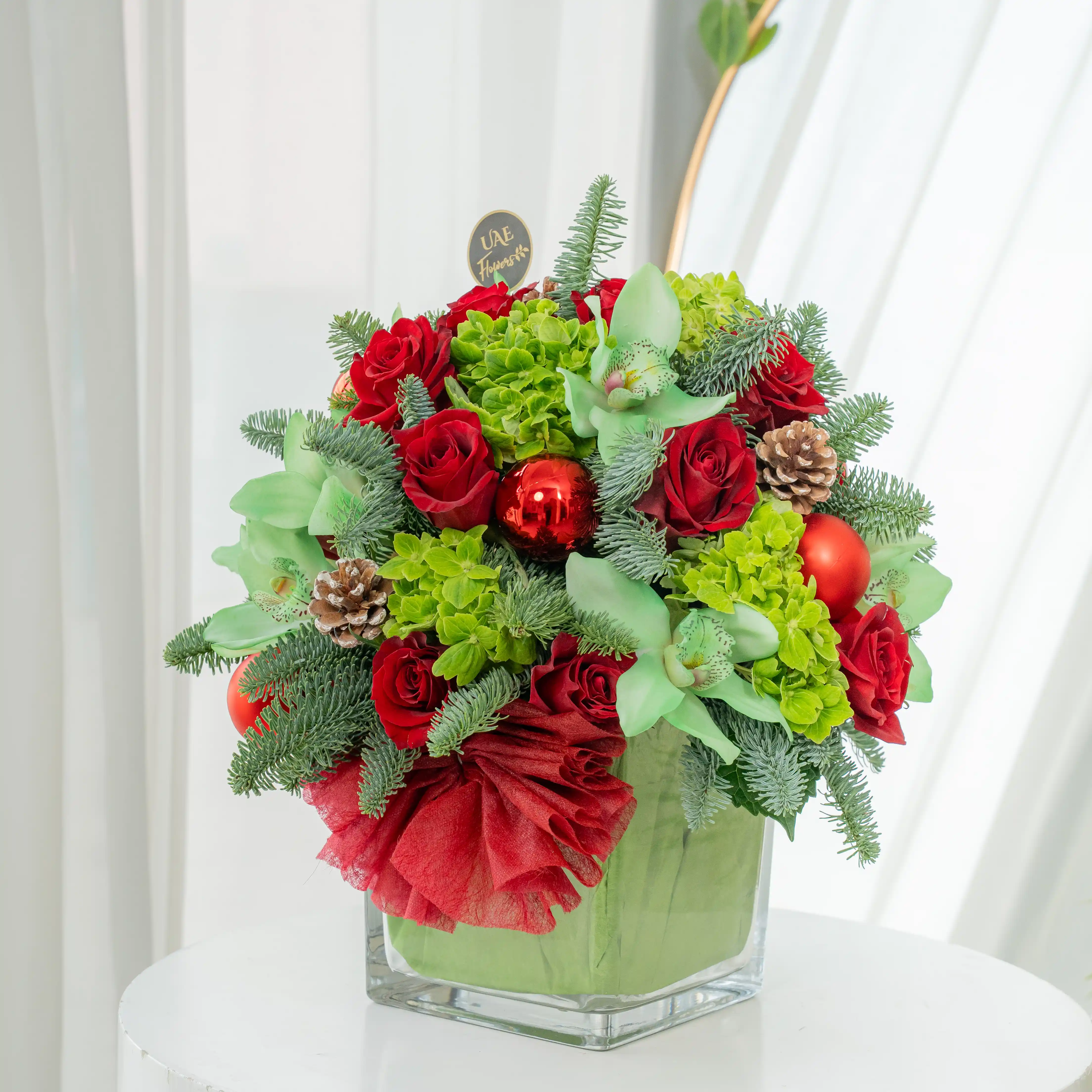 10 red roses, 1 green hydrangea, 1 green cymbidium orchid, Ornaments balls, pinecones, and fillers in a glass vase