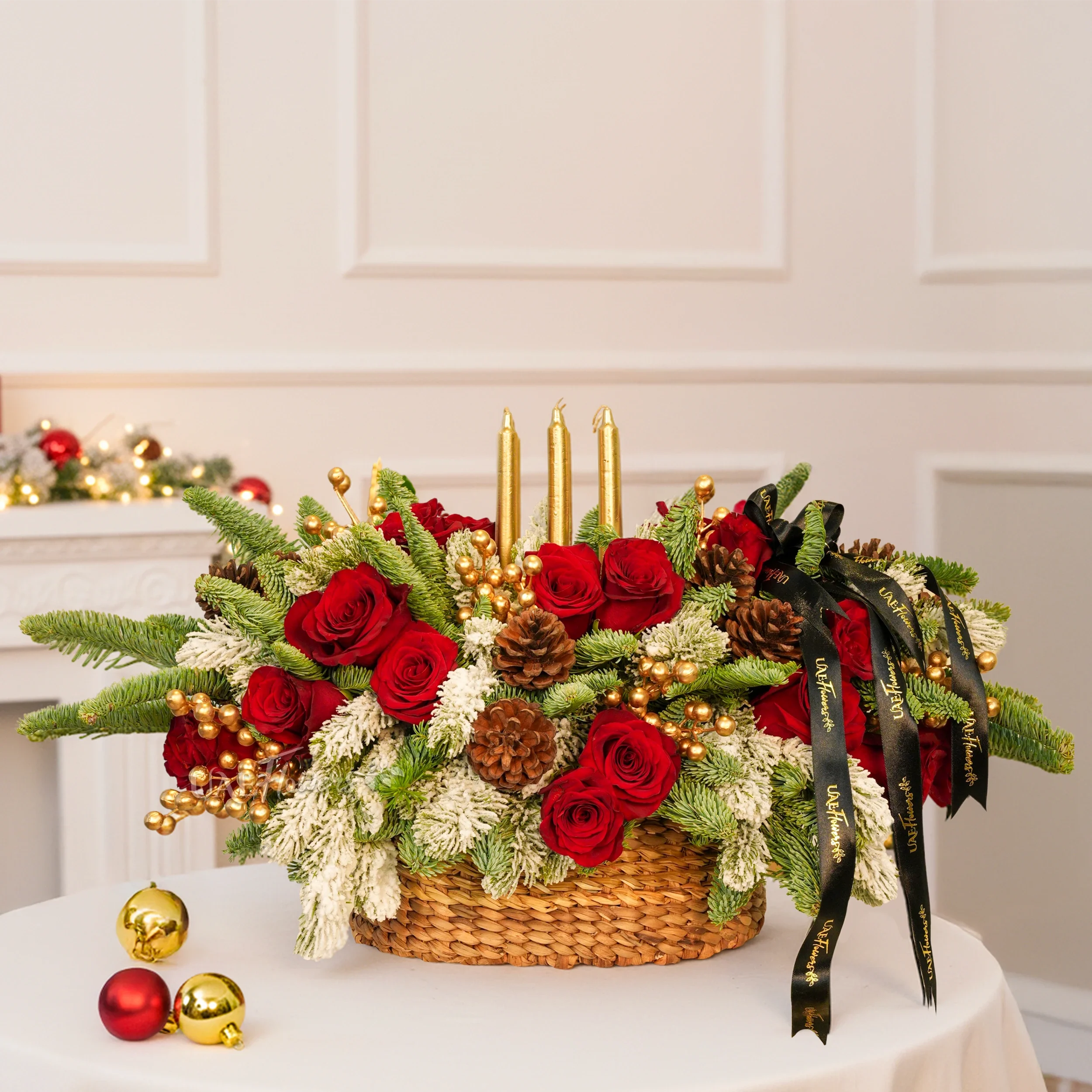 Christmas centerpiece with red roses, snowy pine, gold candles, pinecones in a woven basket