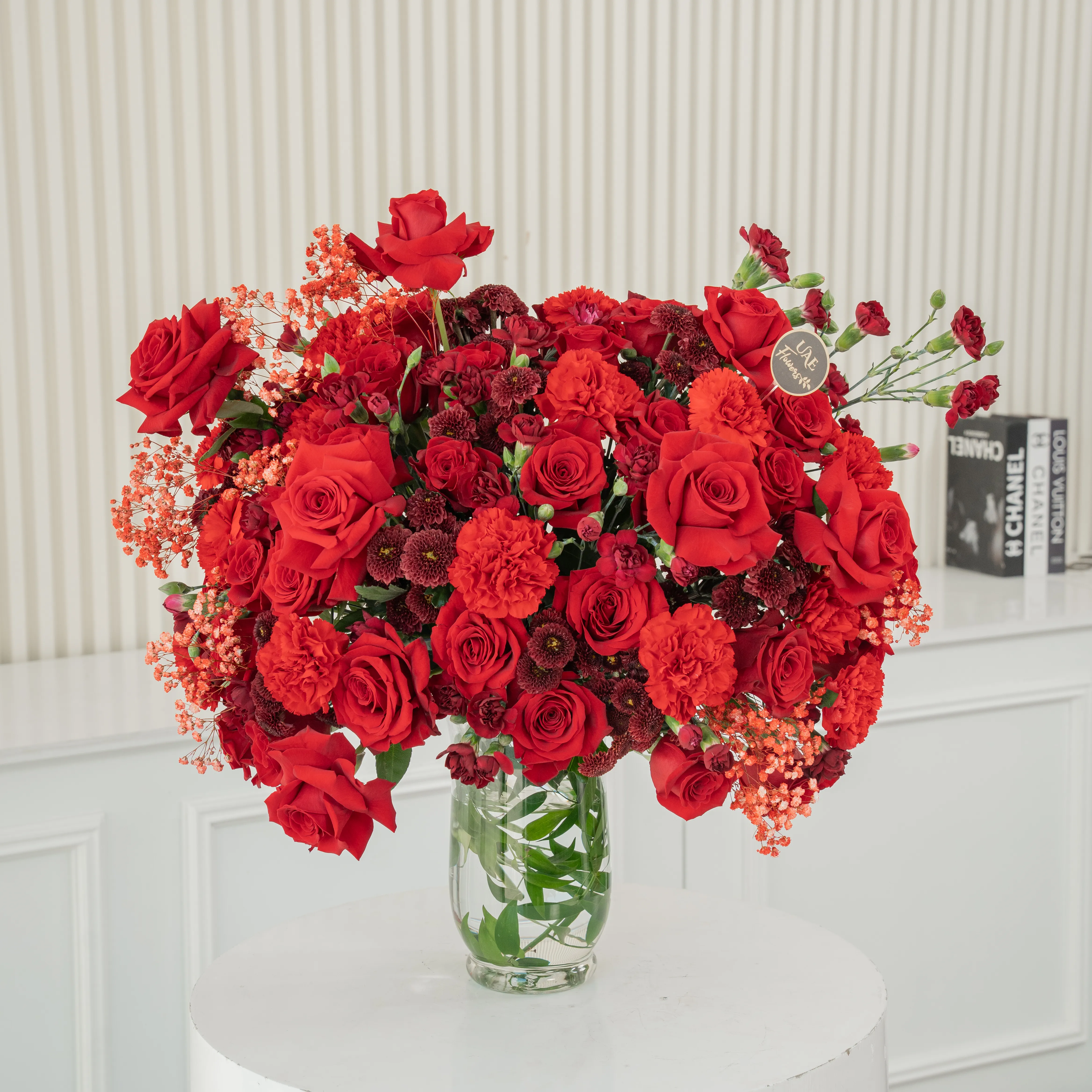 One-side arrangement of 20 red roses, 7 red chrysanthemums, 8 red carnations and 4 red spray carnations with green fillers in a glass vase.