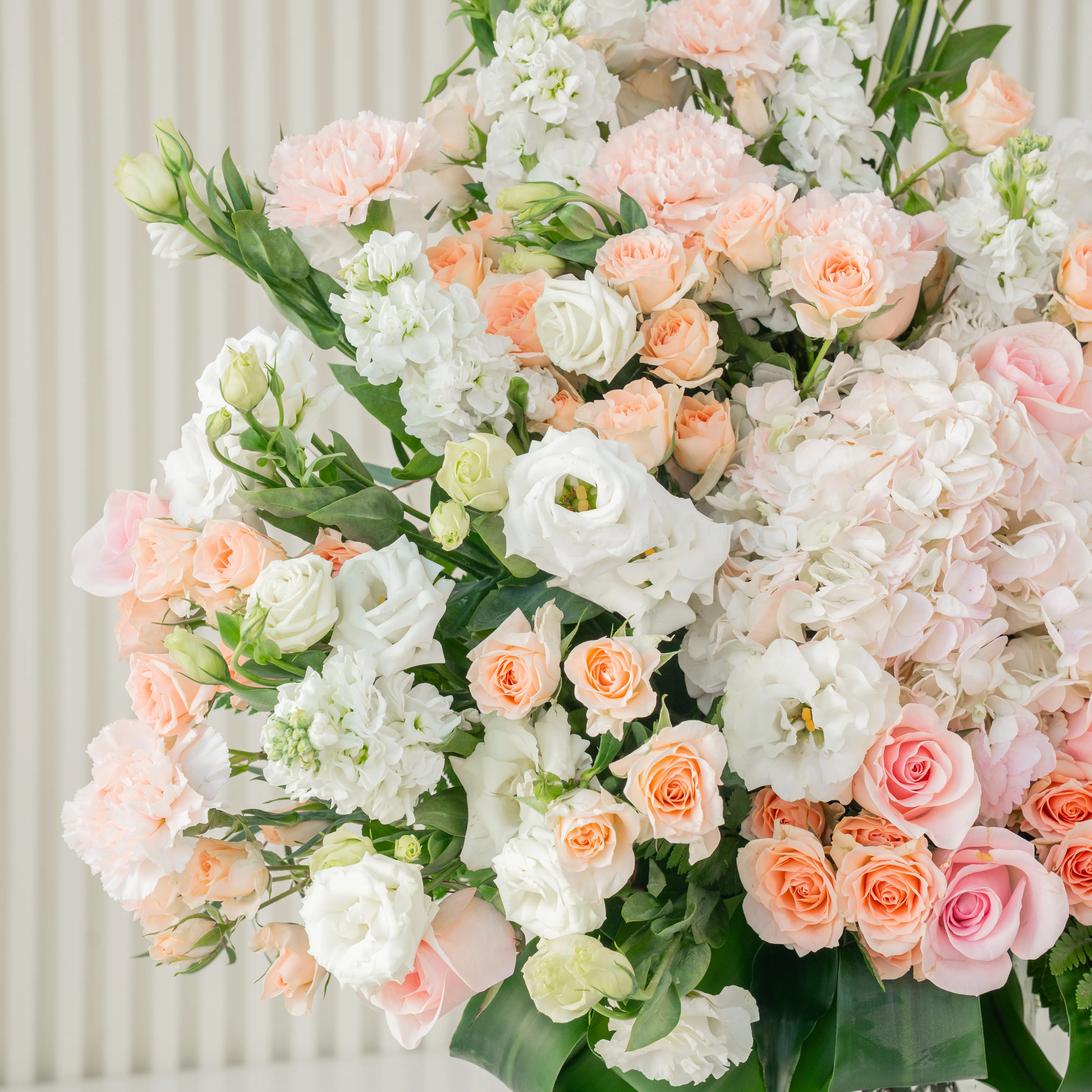 10 white lisianthus, 10 white matthiola, 10 peach roses, 10 pink carnations, 15 pink spray roses and 3 pink hydrangeas with green fillers in a glass vase.