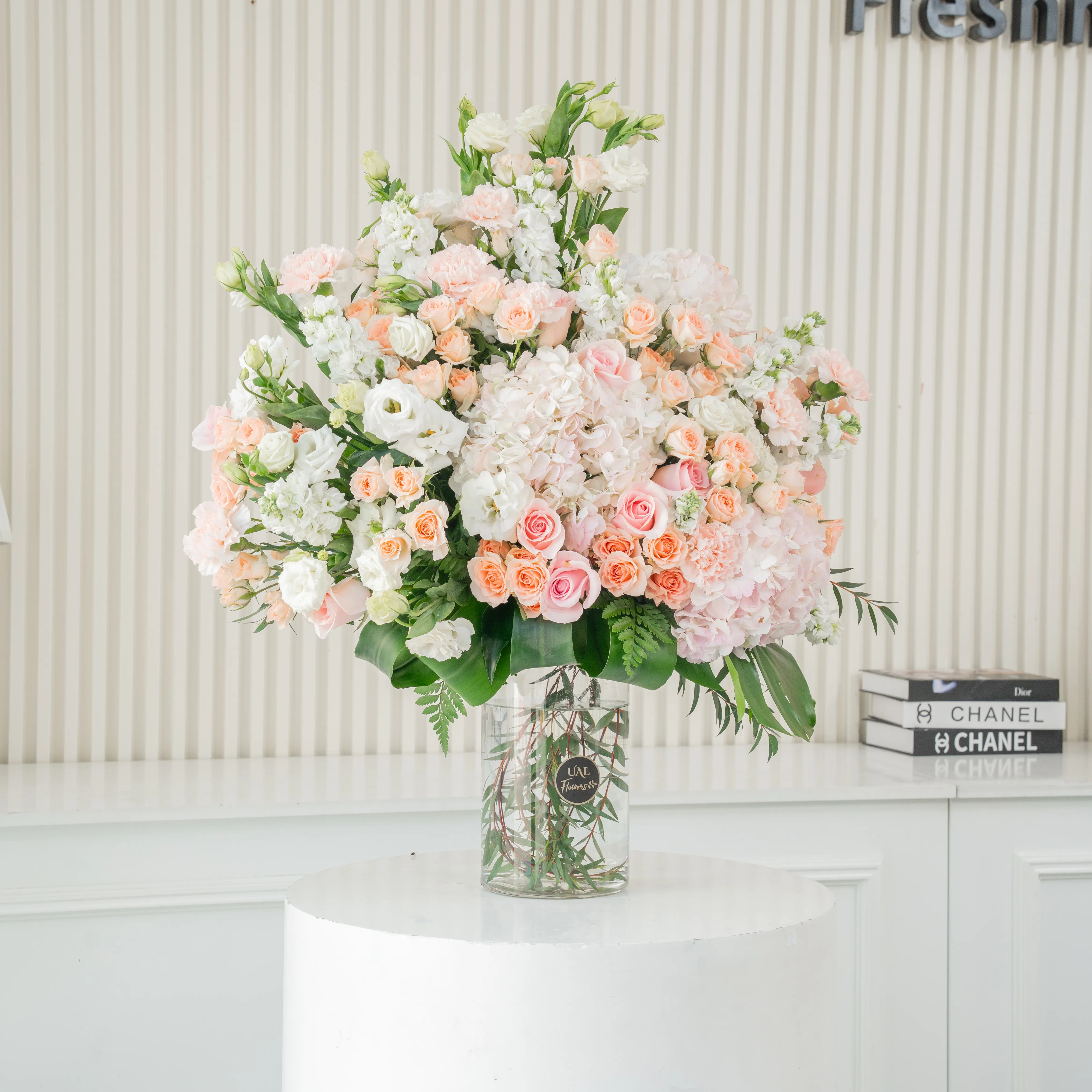 10 white lisianthus, 10 white matthiola, 10 peach roses, 10 pink carnations, 15 pink spray roses and 3 pink hydrangeas with green fillers in a glass vase.