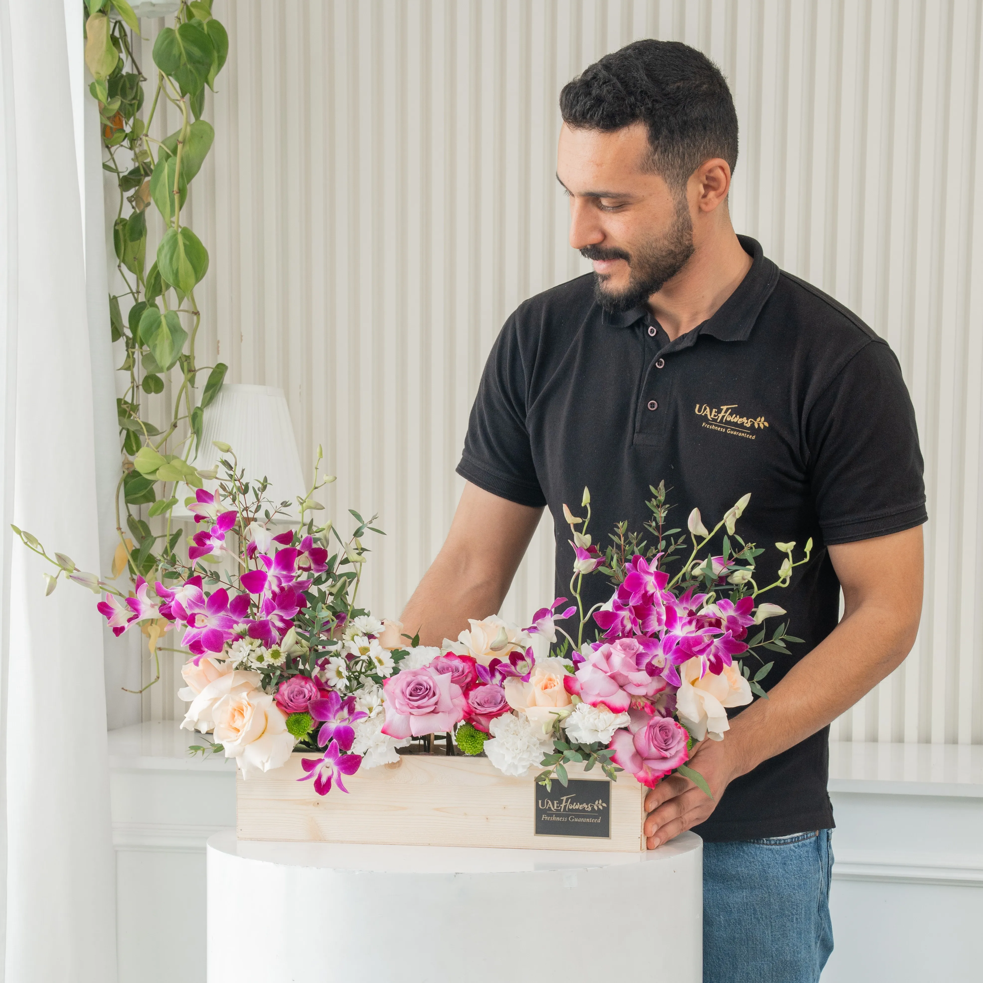 6 purple roses, 6 peach roses, 5 white carnations, 2 white chrysanthemums and 6 purple orchids in a wooden tray.