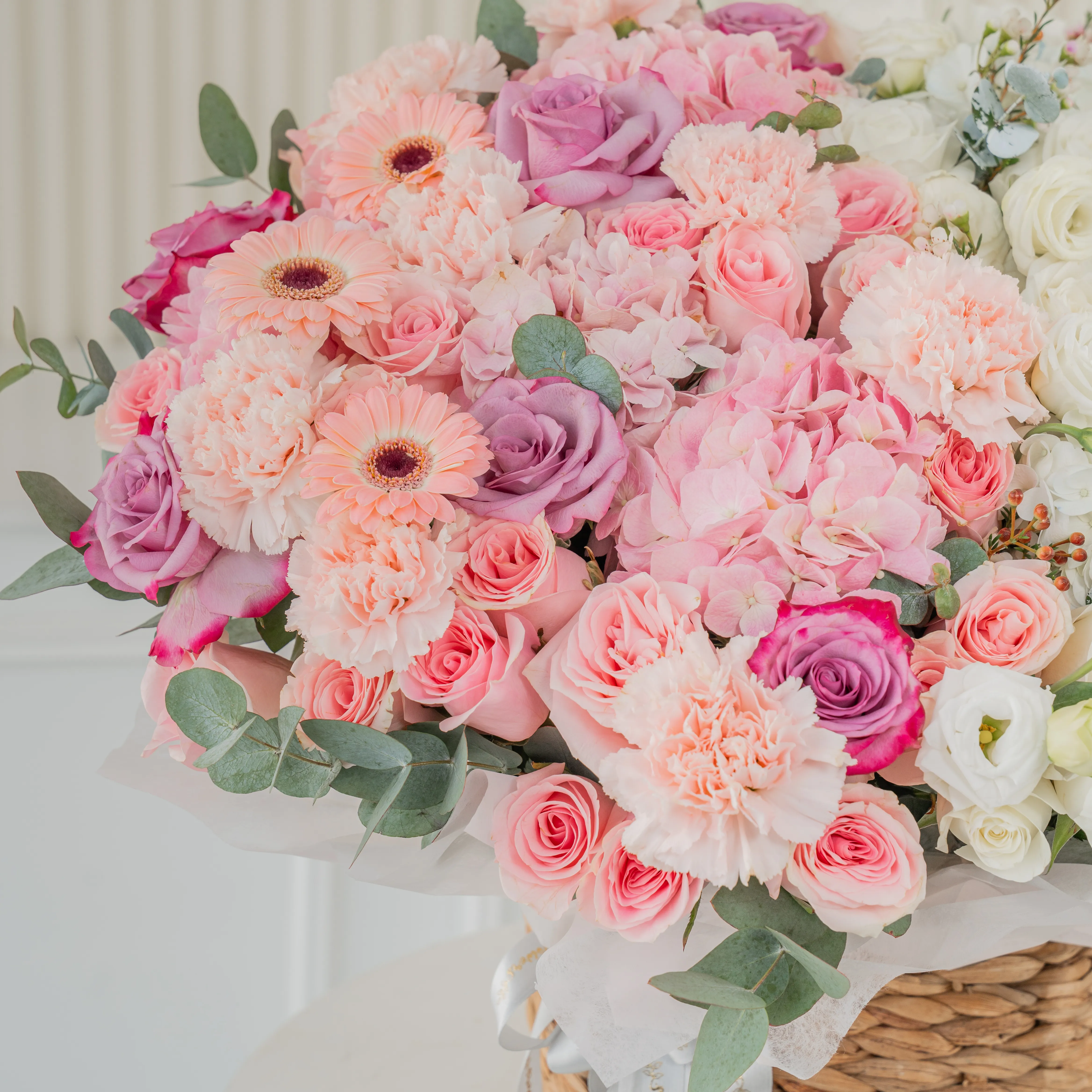 3 pink hydrangeas, 10 pink roses, 10 purple roses, 10 pink carnations, 3 pink gerberas, 3 white hydrangeas, 20 white roses and 7 white lisianthus with green fillers in a basket.