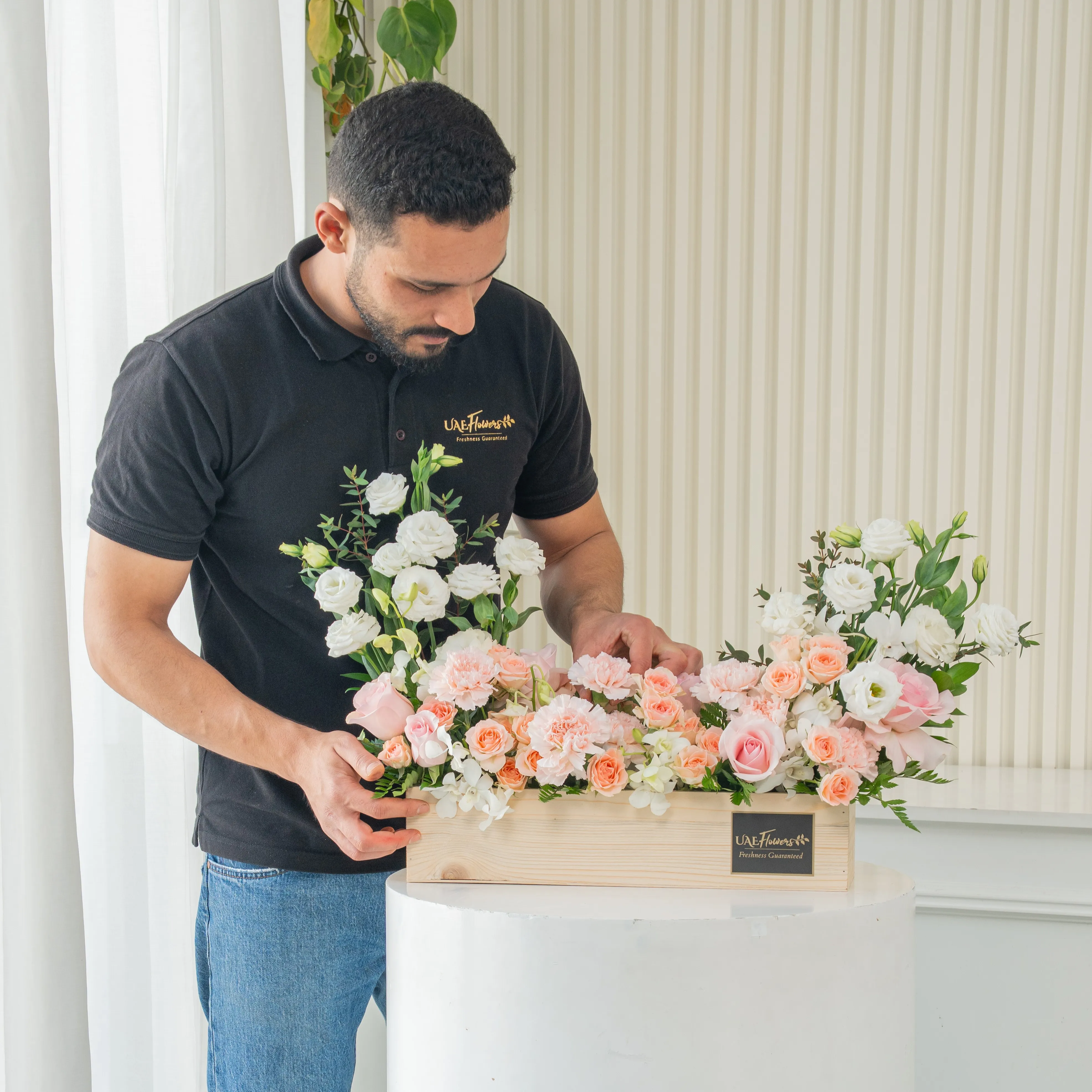 5 pink roses, 6 pink carnations, 3 pink spray roses, 3 white lisianthus and 2 white orchids with green fillers in a wooden tray.