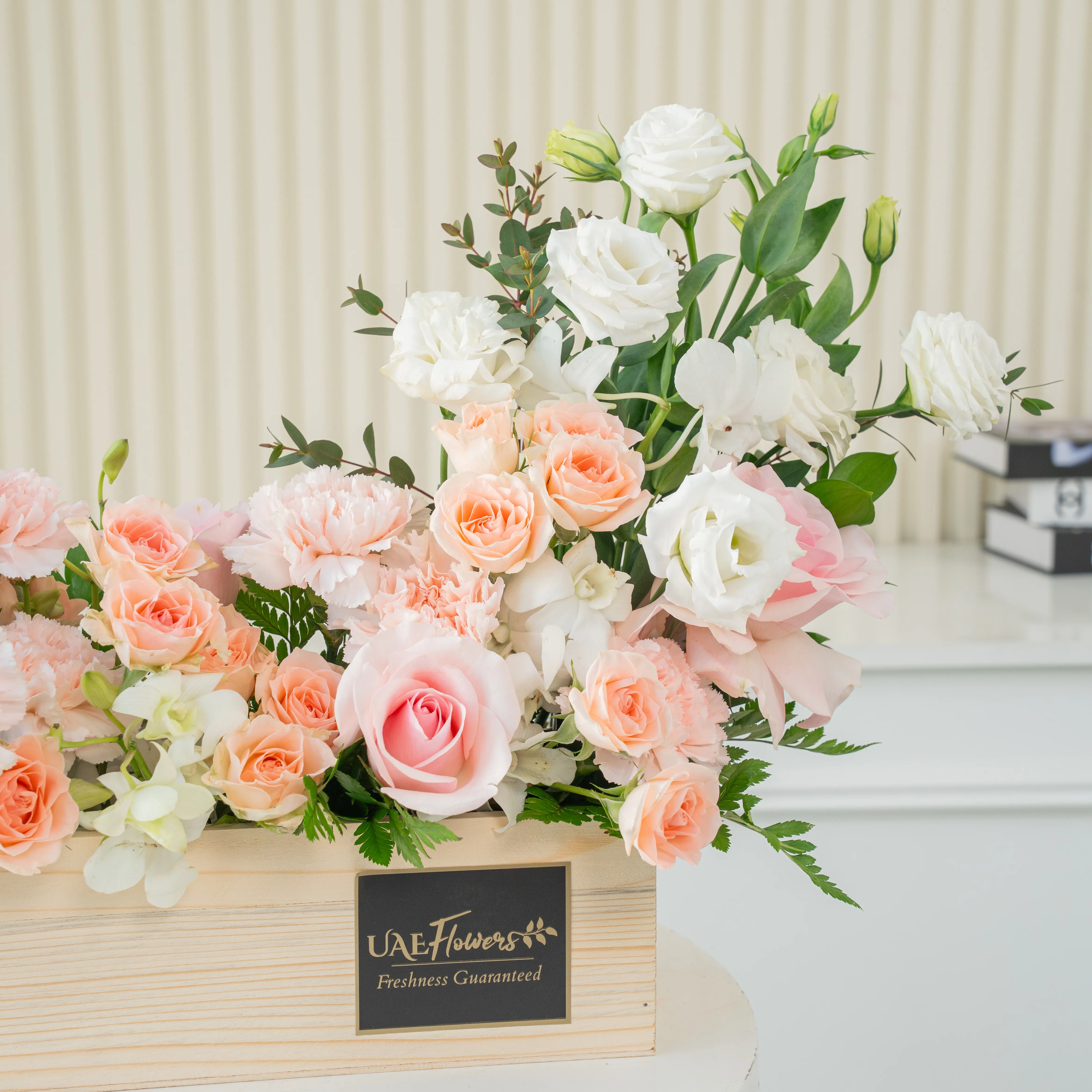 5 pink roses, 6 pink carnations, 3 pink spray roses, 3 white lisianthus and 2 white orchids with green fillers in a wooden tray.