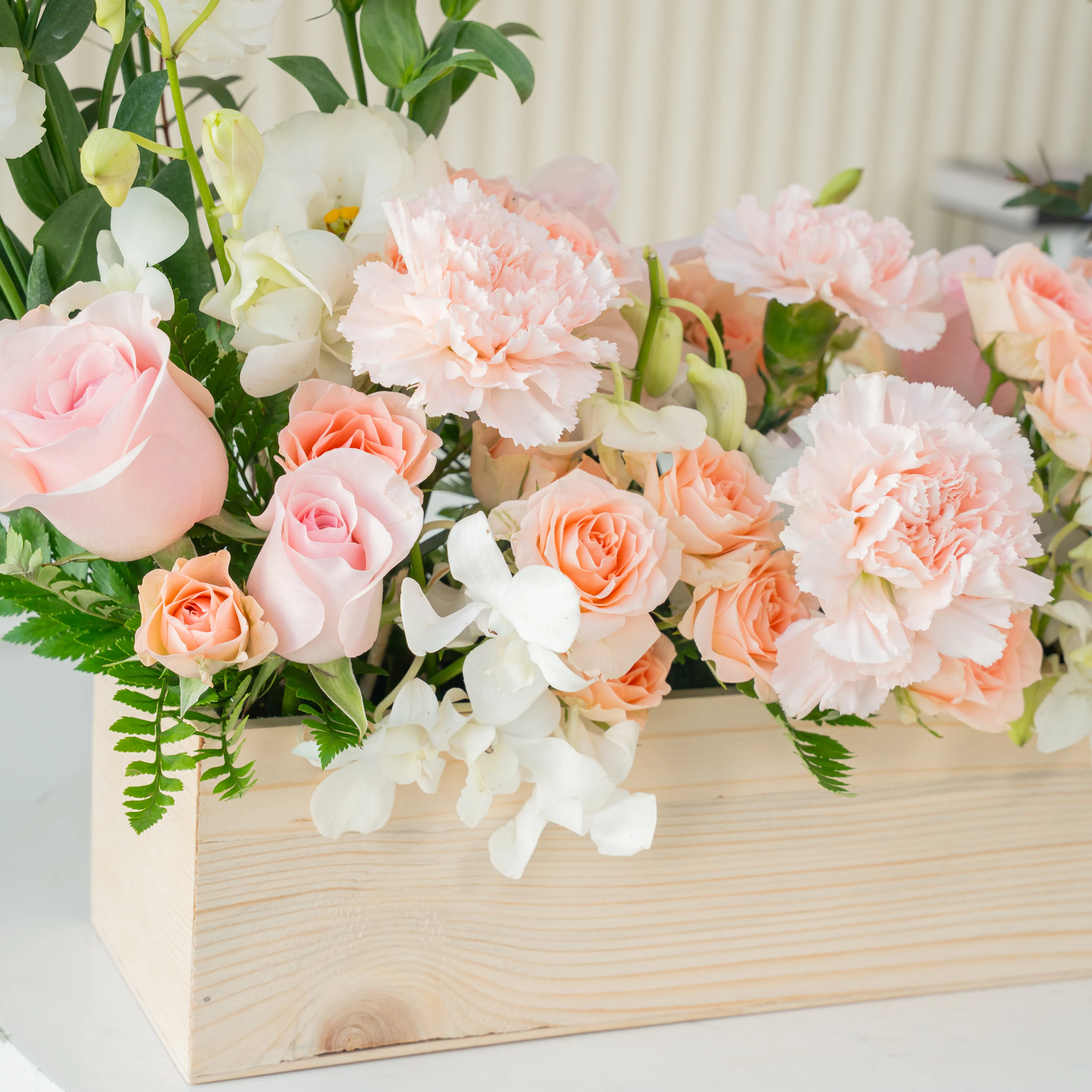 5 pink roses, 6 pink carnations, 3 pink spray roses, 3 white lisianthus and 2 white orchids with green fillers in a wooden tray.