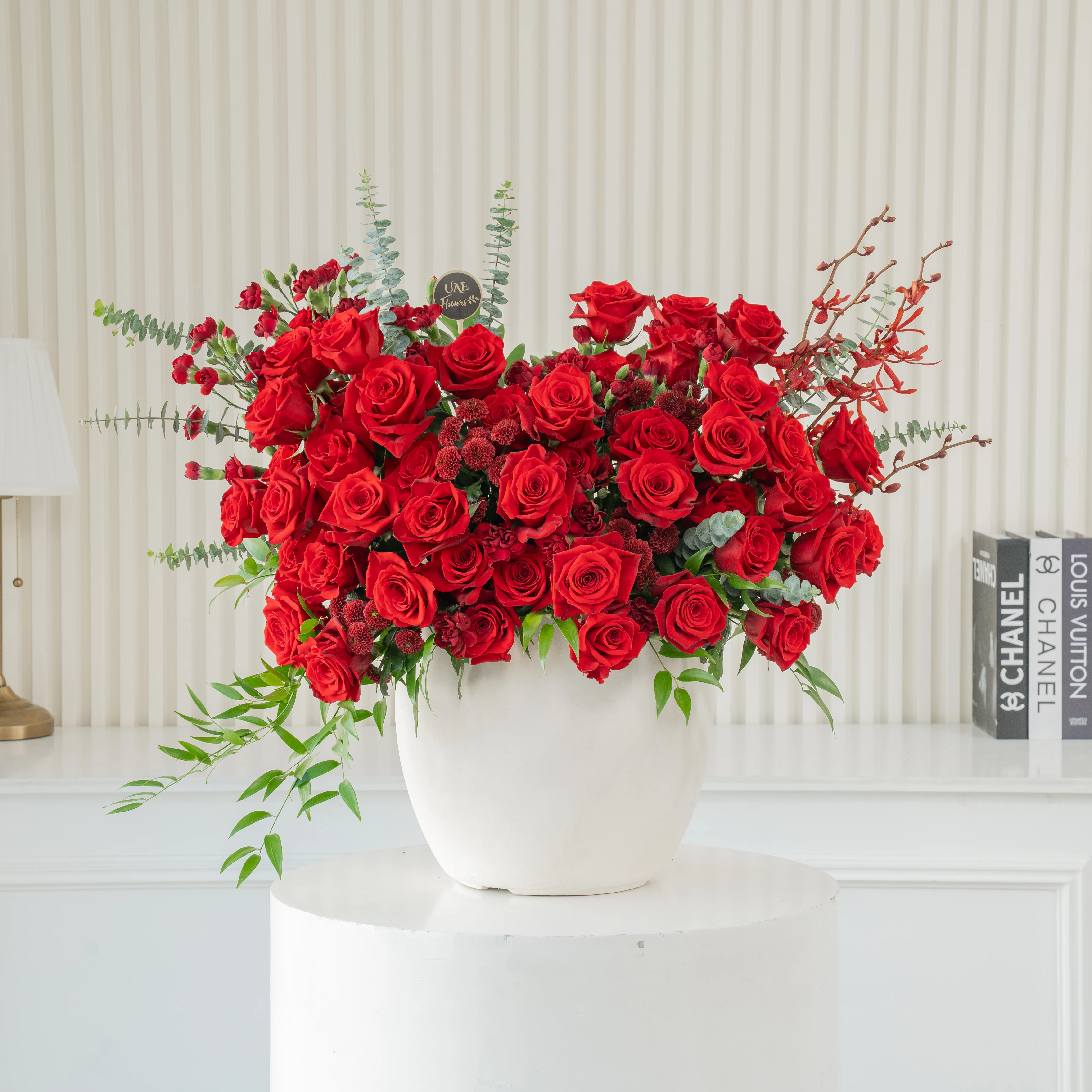 One-side arrangement of 50 red roses, 5 red spray carnations, 5 maroon button chrysanthemums & 4 Black Annie Orchids with green fillers in a ceramic vase.