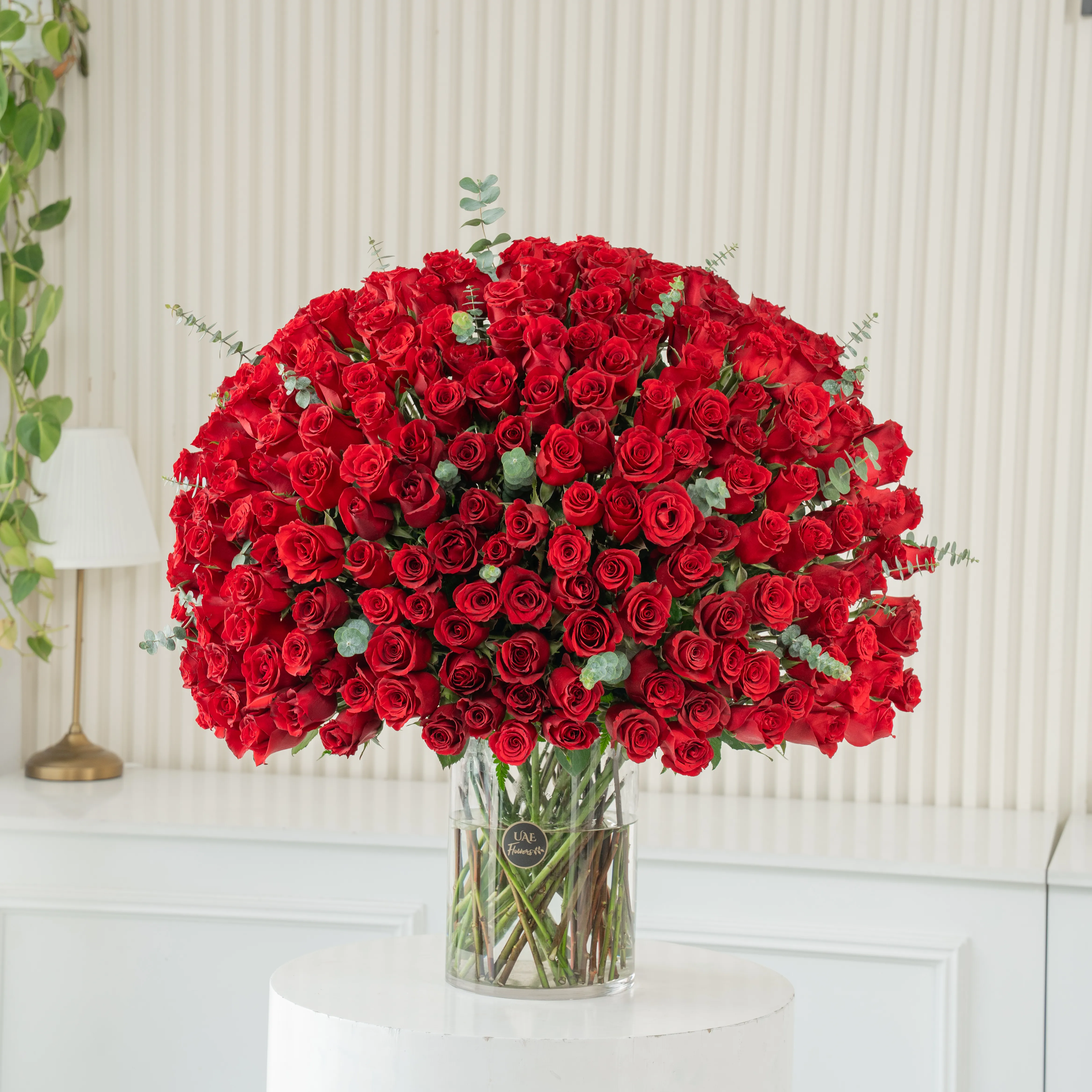 200 red roses with green fillers in a glass vase.