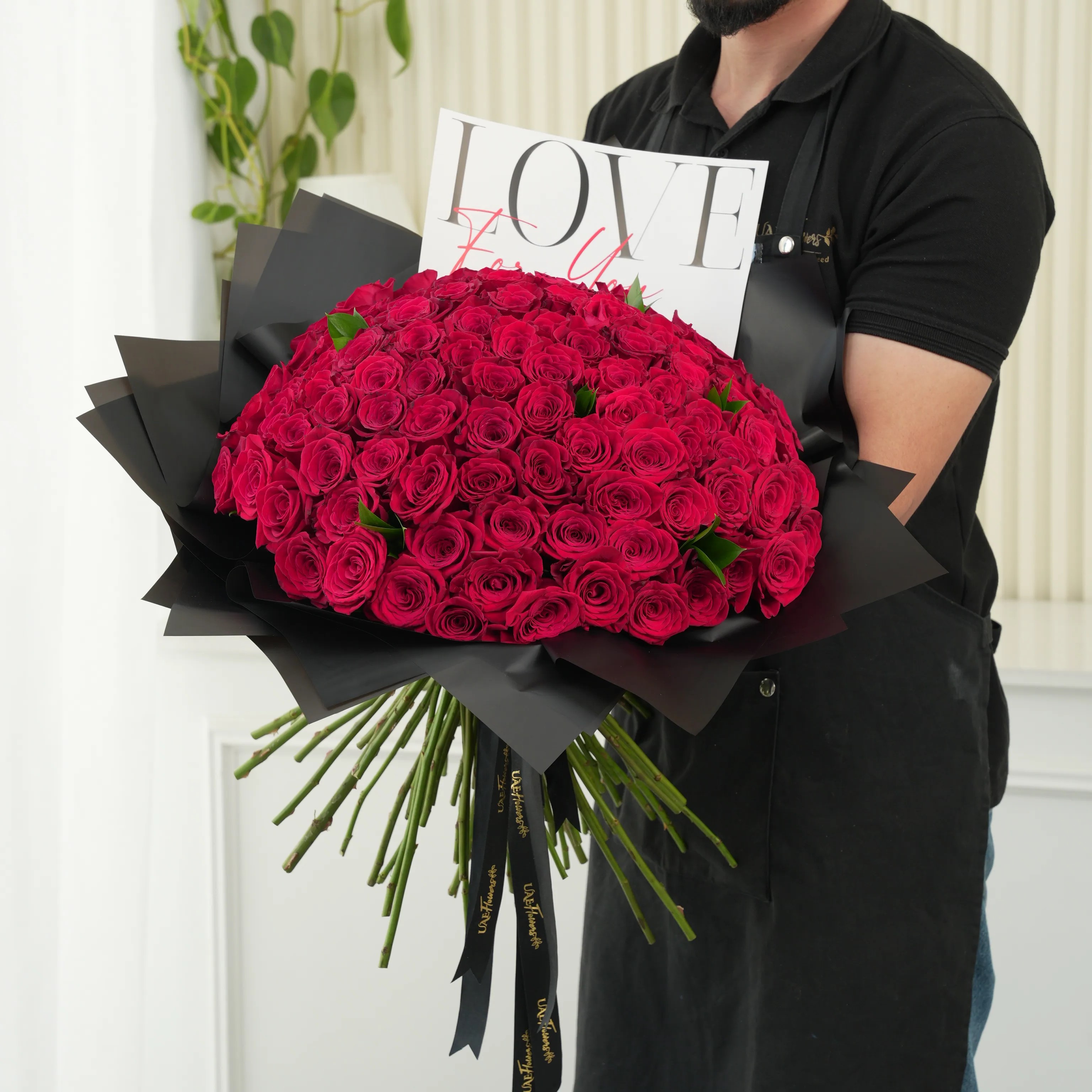 100 red roses with green fillers in black wrapping with Love For You Paper tied with black ribbons.