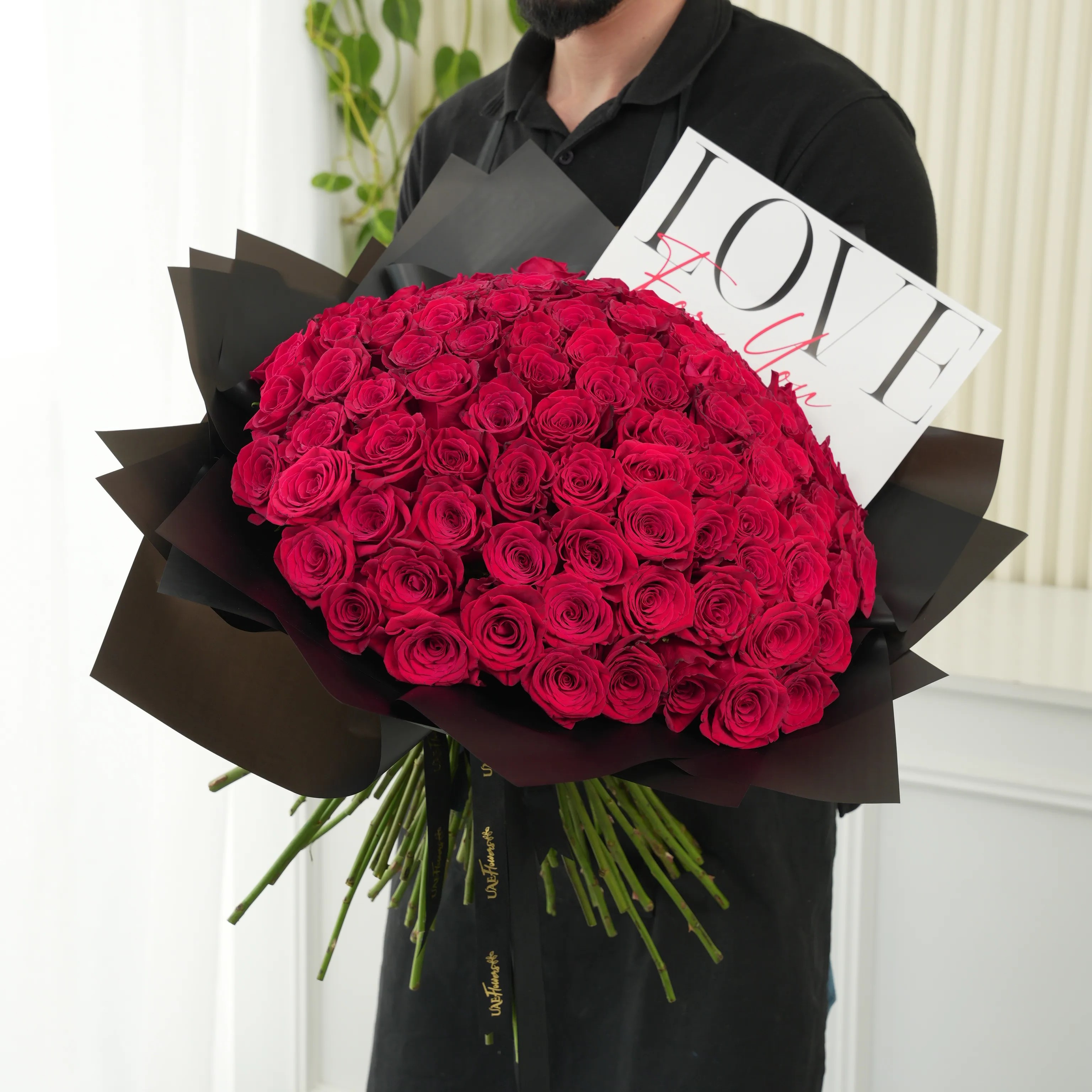 100 red roses with green fillers in black wrapping with Love For You Paper tied with black ribbons.