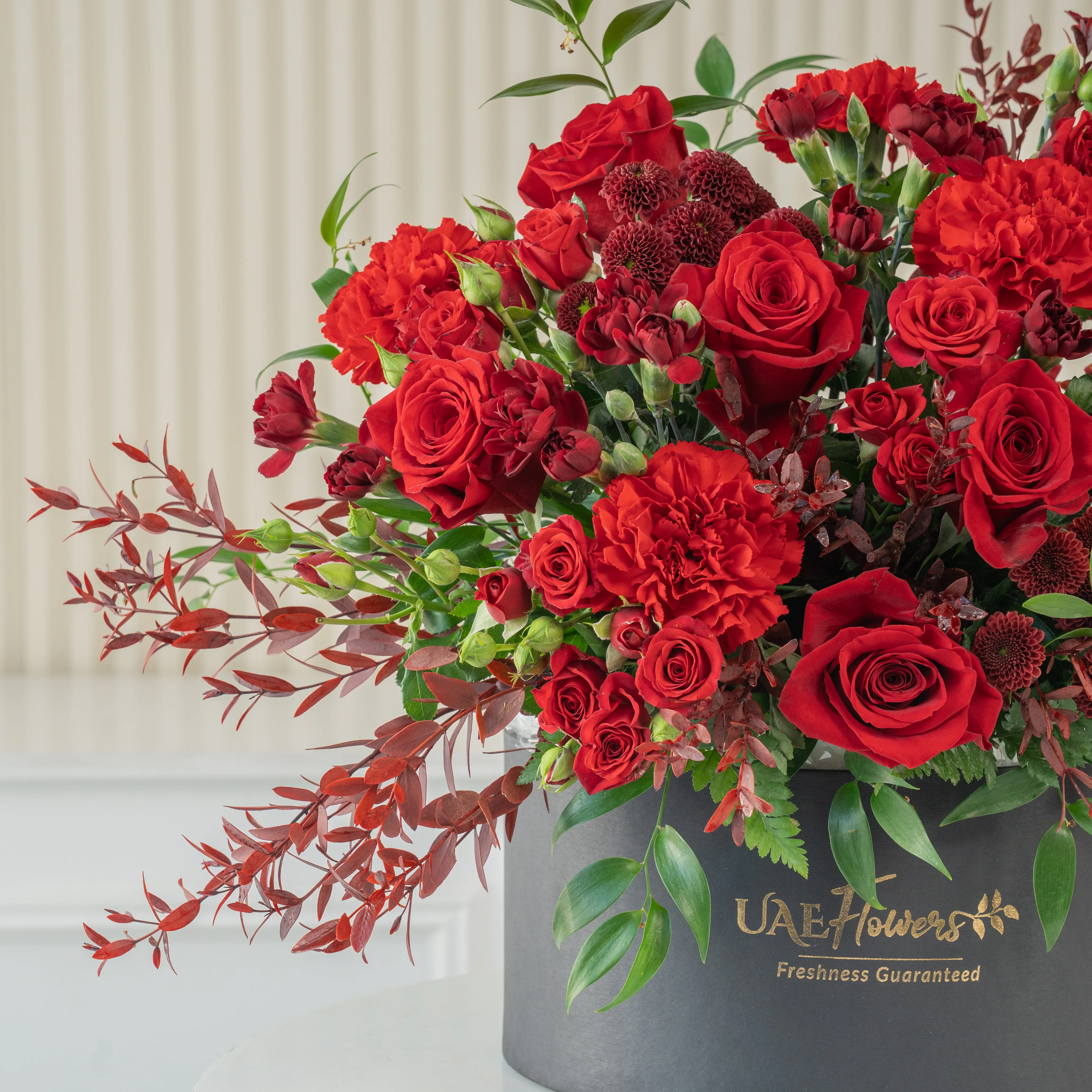 4 annie black orchids, 8 red roses, 3 red spray roses, 2 red chrysanthemums and 4 red spray carnations with green fillers in a round box.