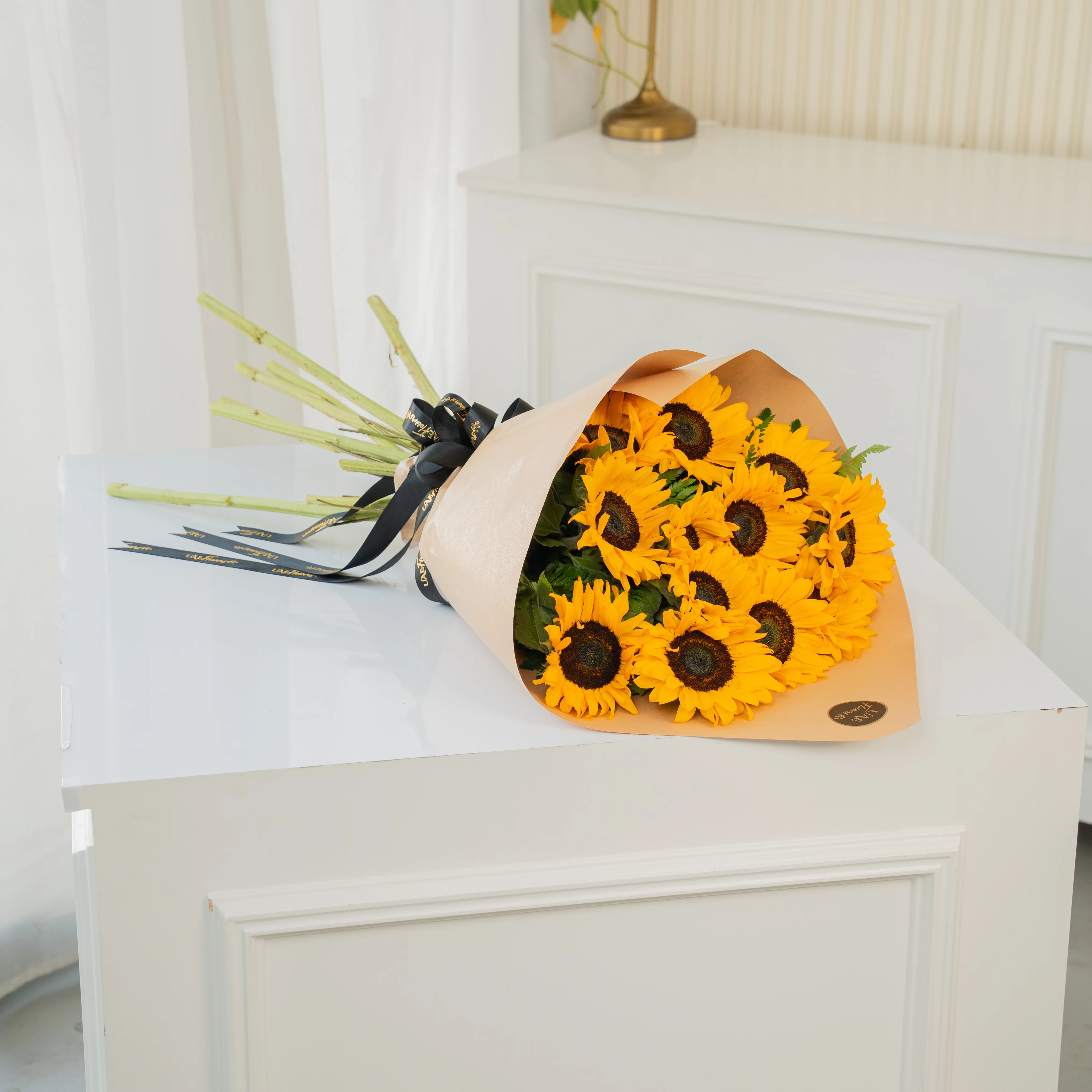 Bouquet of 12 sunflowers in paper packing hand-tied with ribbons.