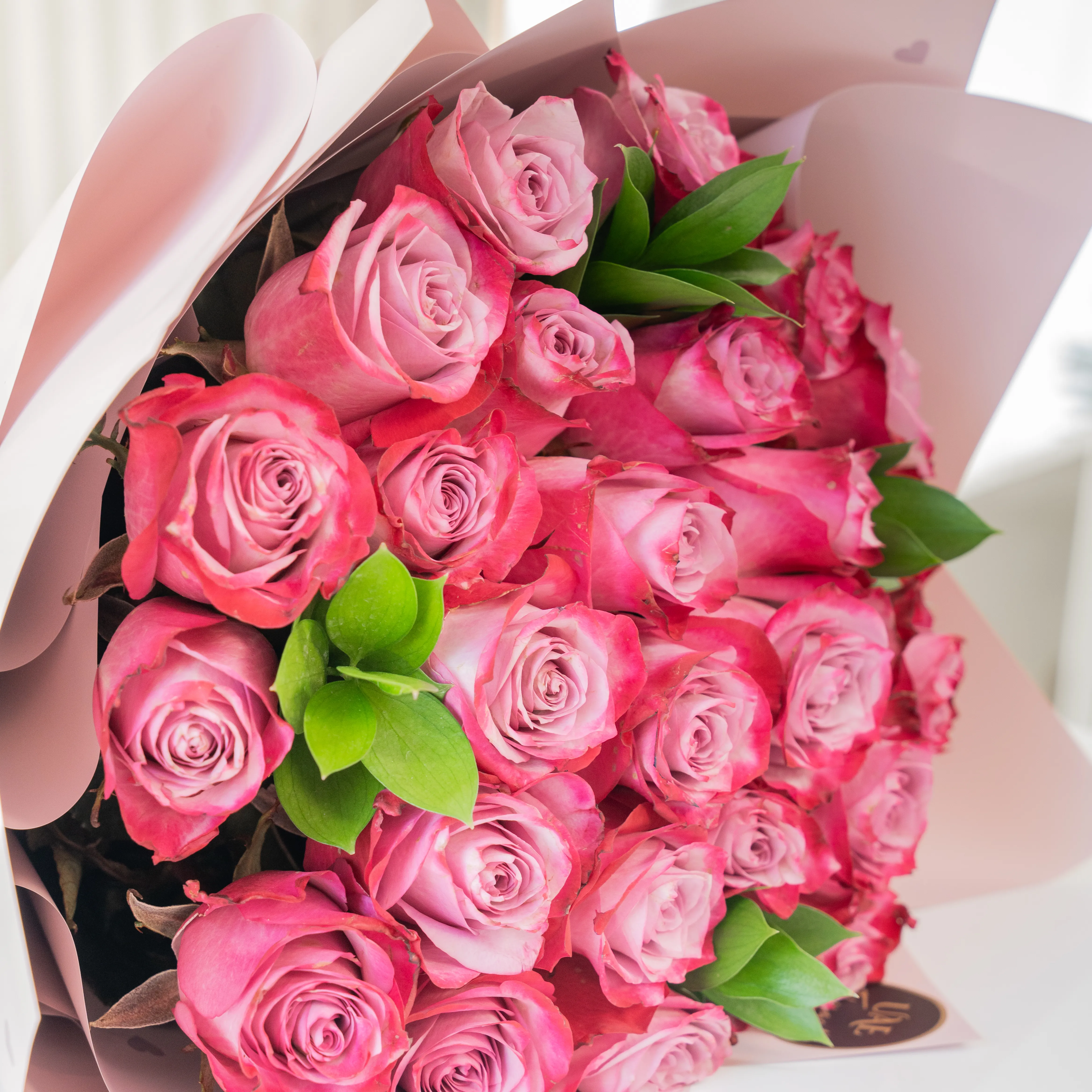Bouquet of 20 purple roses in paper packing hand-tied with ribbons.