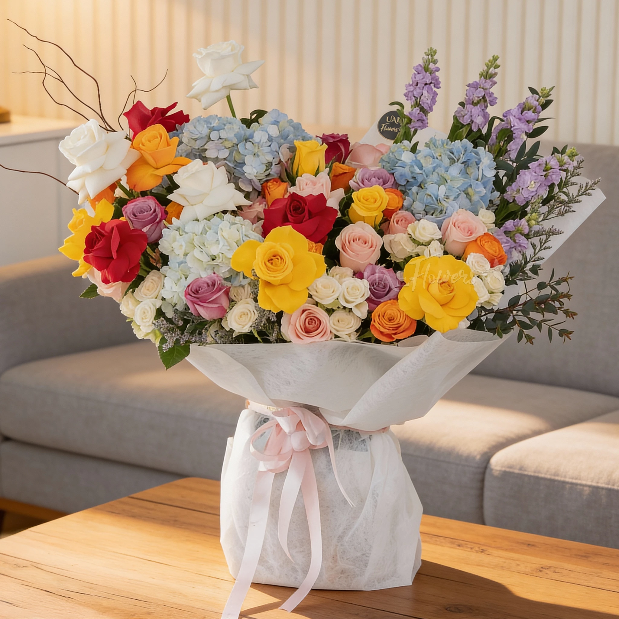 Bouquet of 25 mix roses, 6 white spray roses, 3 blue hydrangeas and 5 purple matthiola with green fillers in white paper packing tied with pink ribbon.