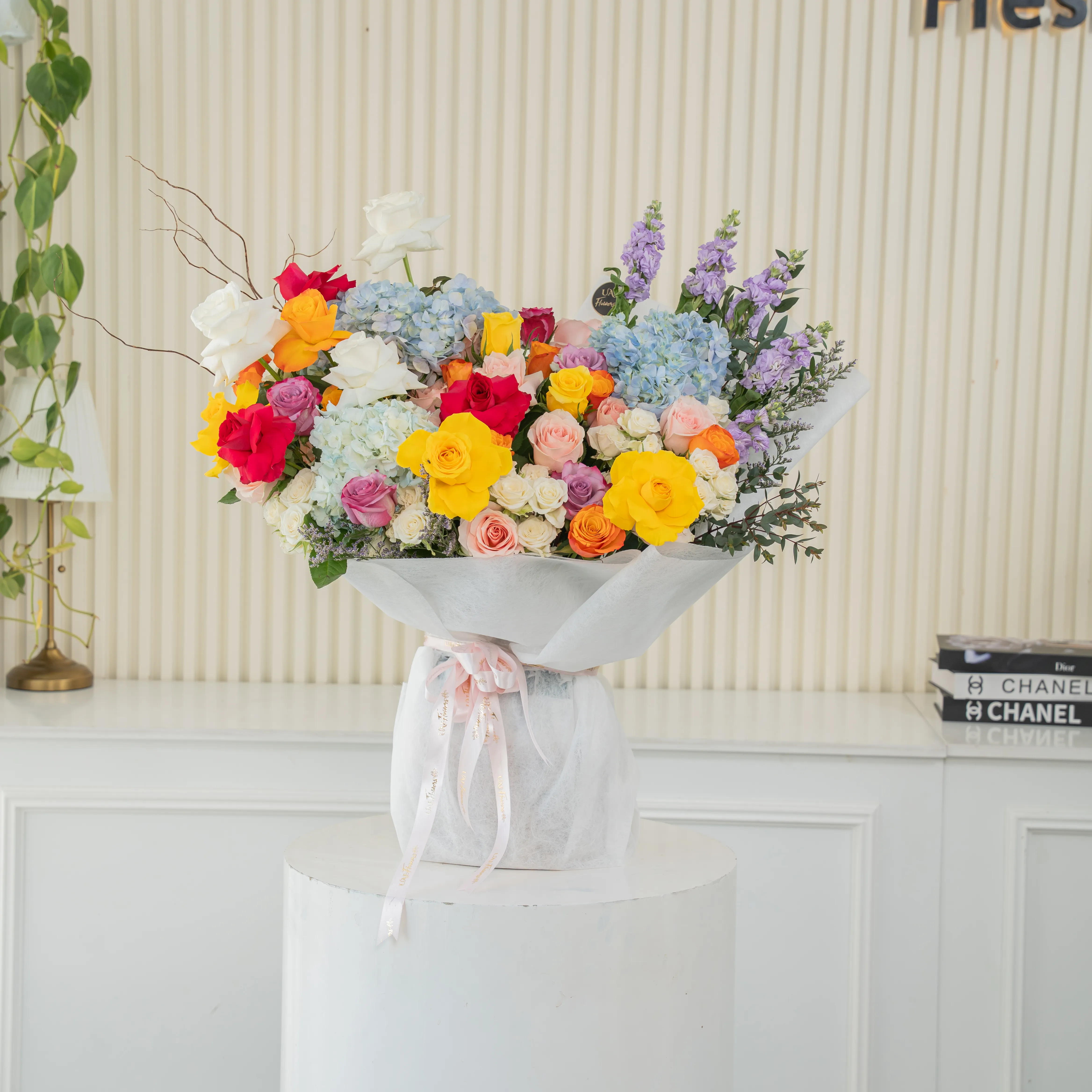 Bouquet of 25 mix roses, 6 white spray roses, 3 blue hydrangeas and 5 purple matthiola with green fillers in white paper packing tied with pink ribbon.