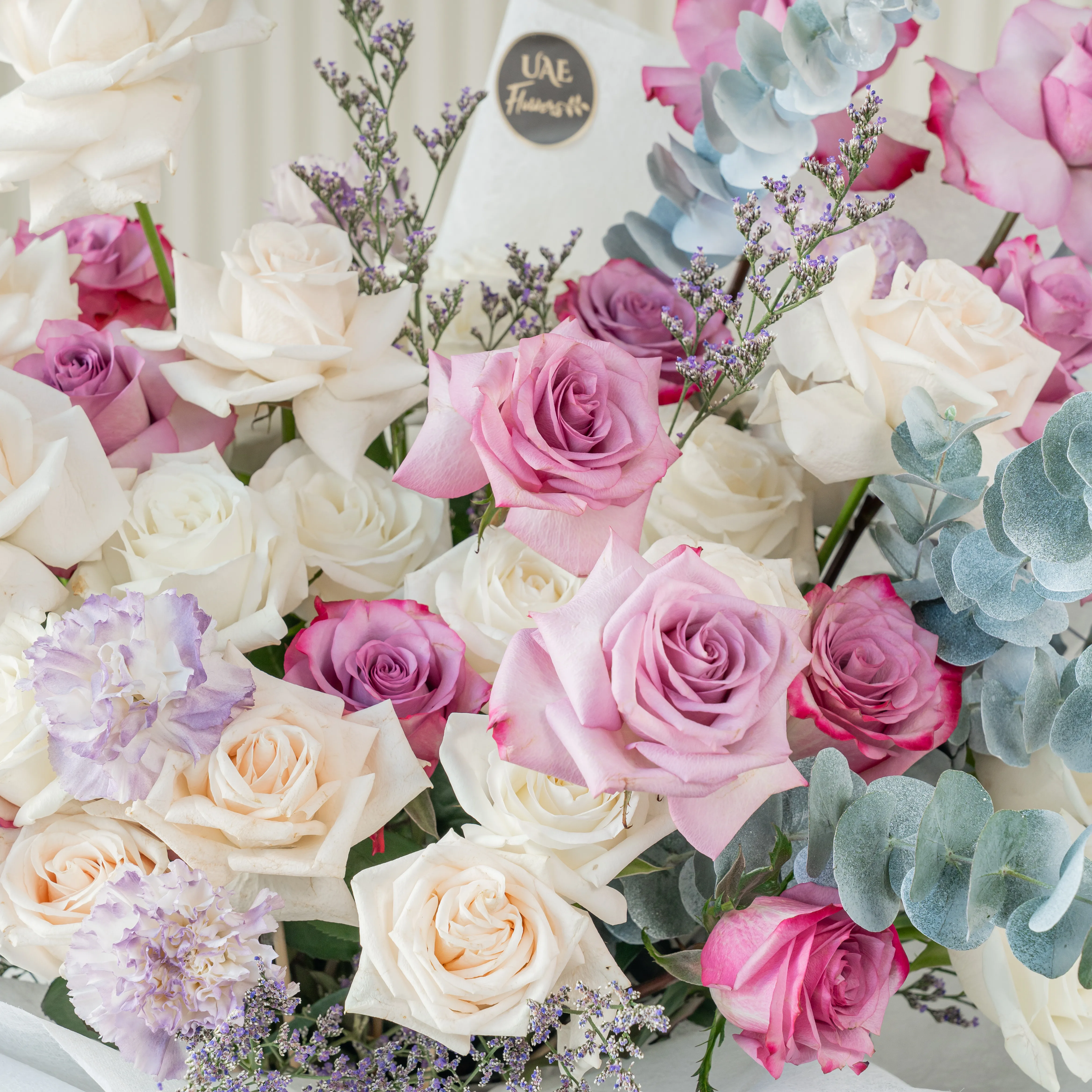 Bouquet of 20 white roses, 12 purple roses and 5 carnations with eucalyptus leaf and green fillers in white paper packing tied with white ribbon.