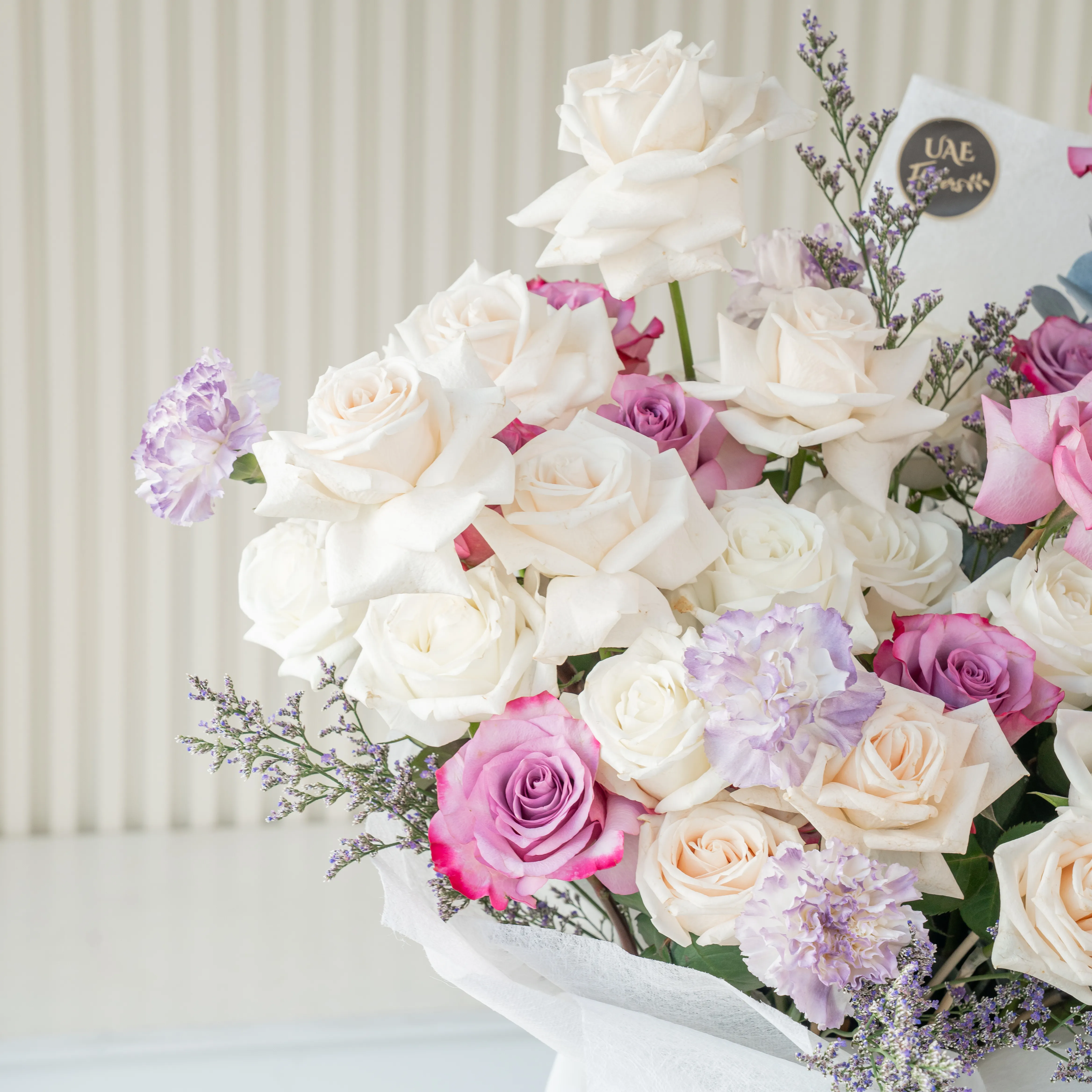 Bouquet of 20 white roses, 12 purple roses and 5 carnations with eucalyptus leaf and green fillers in white paper packing tied with white ribbon.