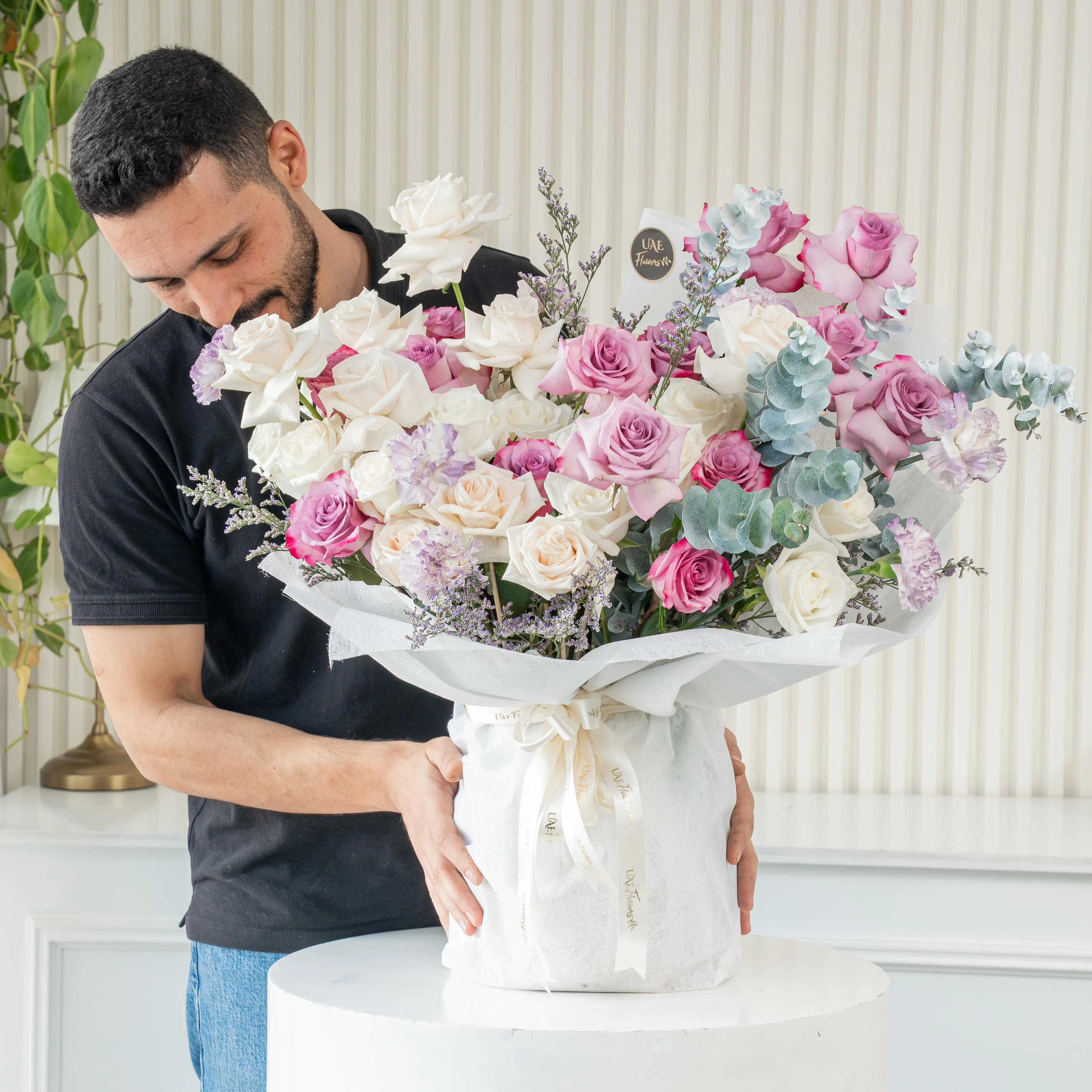 Bouquet of 20 white roses, 12 purple roses and 5 carnations with eucalyptus leaf and green fillers in white paper packing tied with white ribbon.