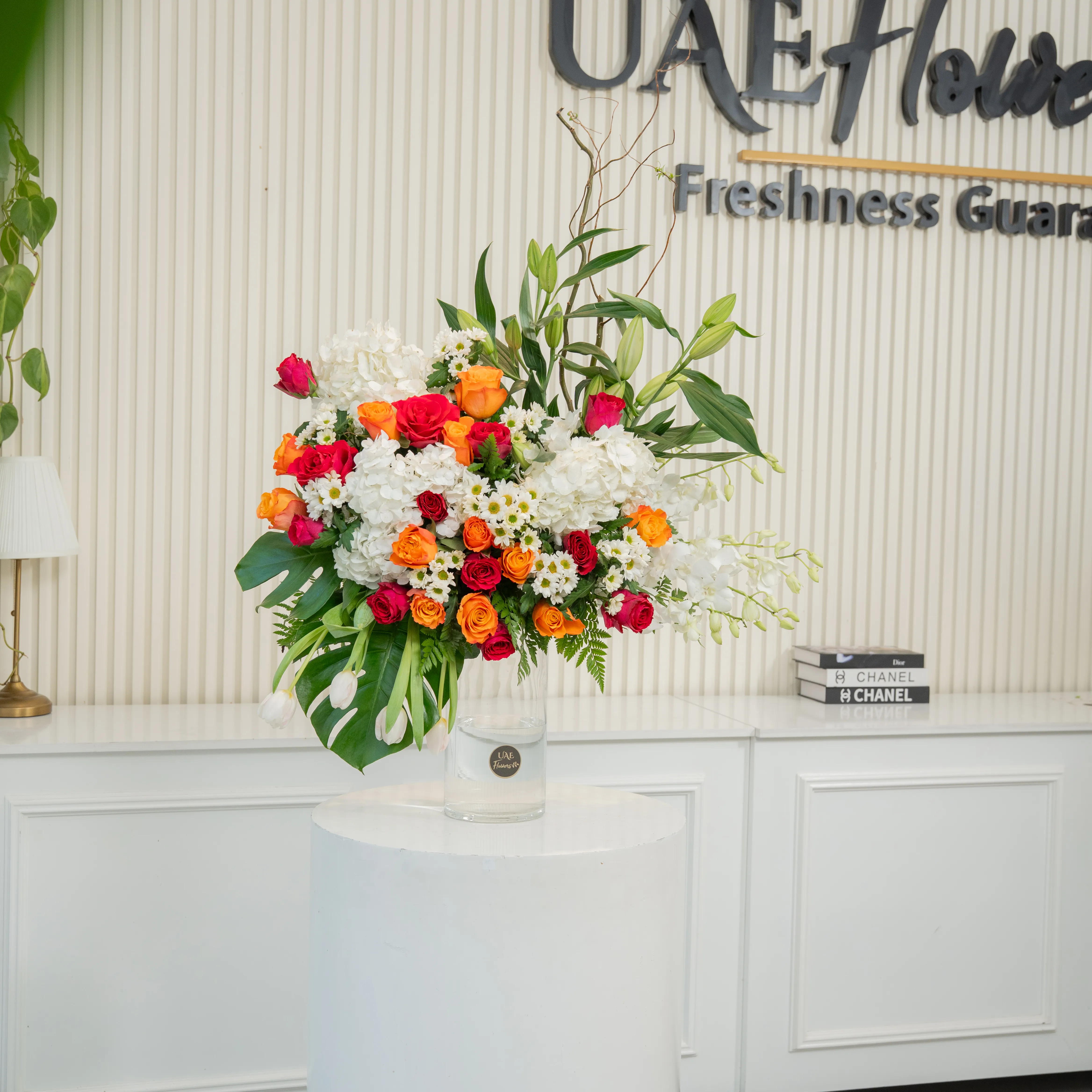 Glass vase arrangement of 3 white lilies, 3 White Hydrangeas, 7 White Orchids, 4 White Tulips, 25 Orange and Red Roses, 6 white Chrysanthemums with green fillers.