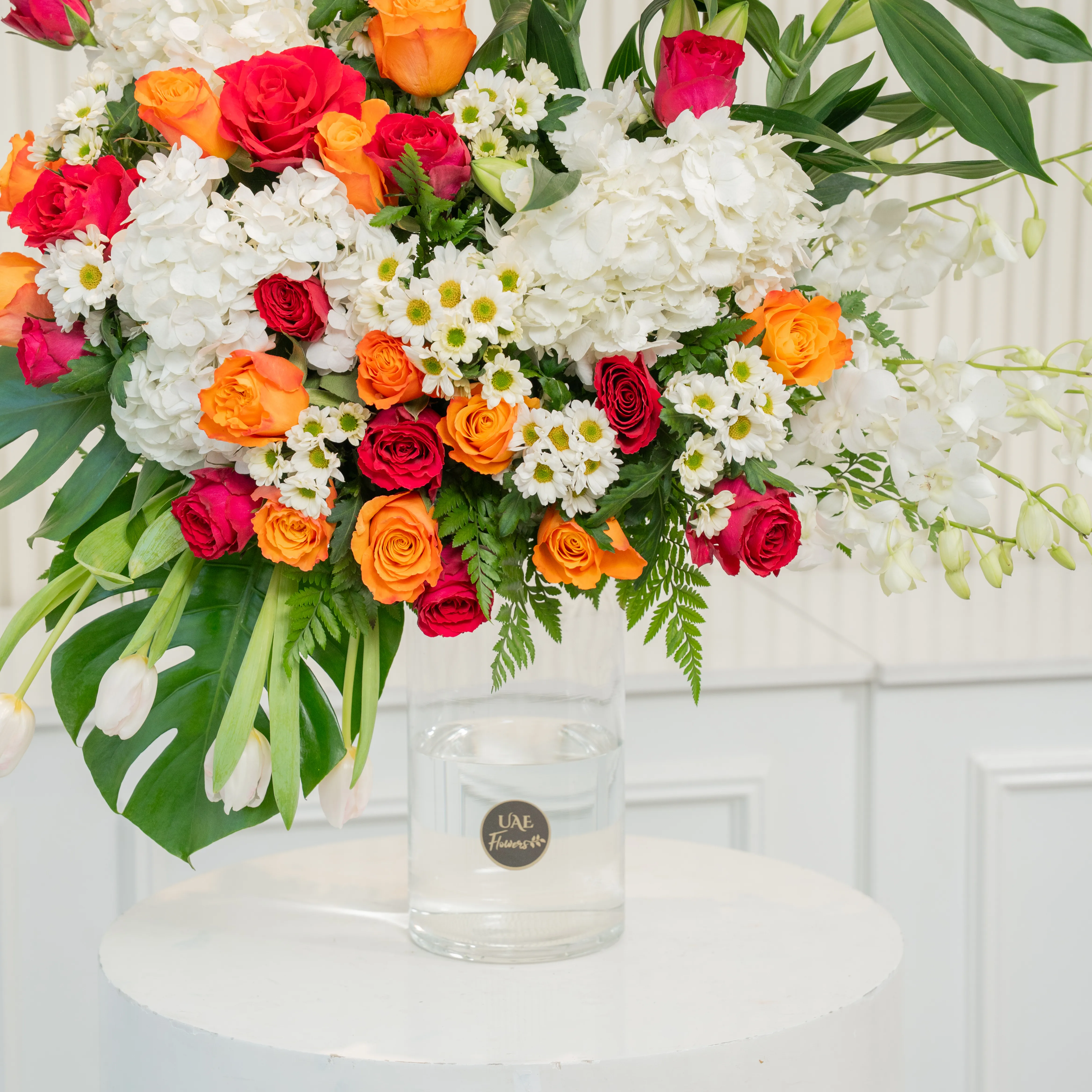 Glass vase arrangement of 3 white lilies, 3 White Hydrangeas, 7 White Orchids, 4 White Tulips, 25 Orange and Red Roses, 6 white Chrysanthemums with green fillers.