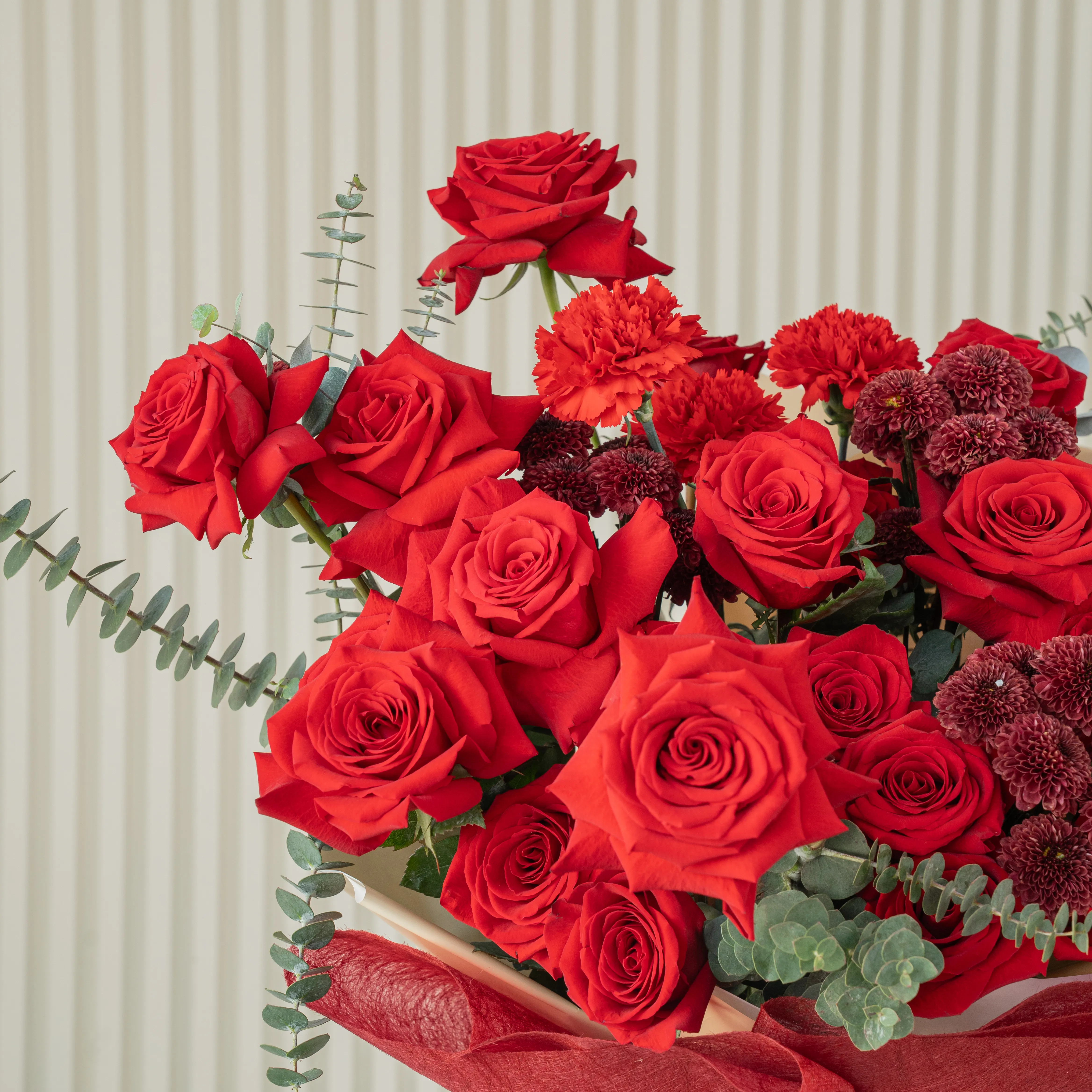 Bouquet of 10 red roses, 5 red spray roses and 3 red button chrysanthemums with eucalyptus leaf in red paper packing tied with black ribbon.