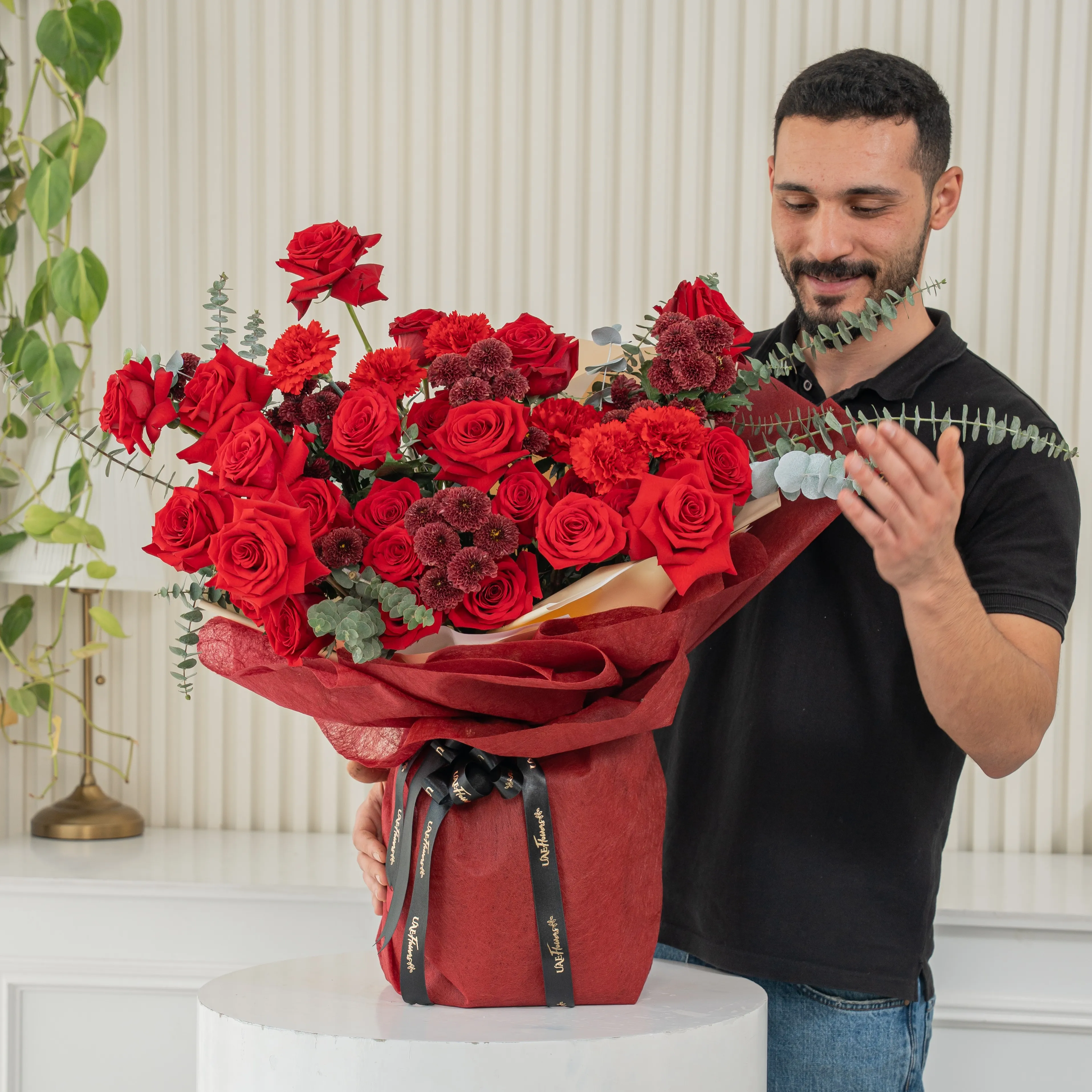 Bouquet of 10 red roses, 5 red spray roses and 3 red button chrysanthemums with eucalyptus leaf in red paper packing tied with black ribbon.