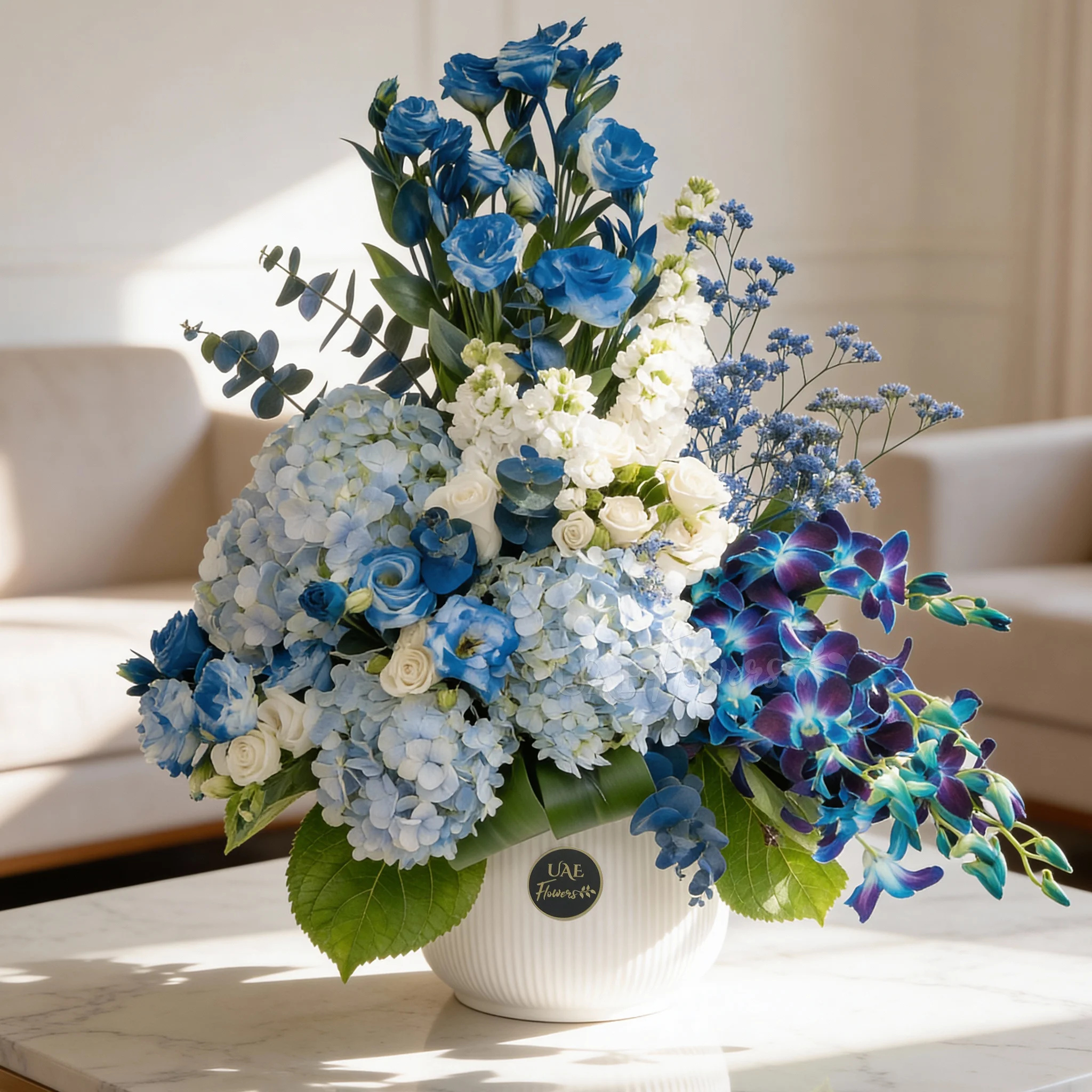 An arrangement of 10 white lisinathus, 5 white matthiola, 10 blue orchids, 5 white roses, 10 white spray roses and 3 blue hydrangeas with eucalyptus leaf and Limonium fillers in a ceramic pot.