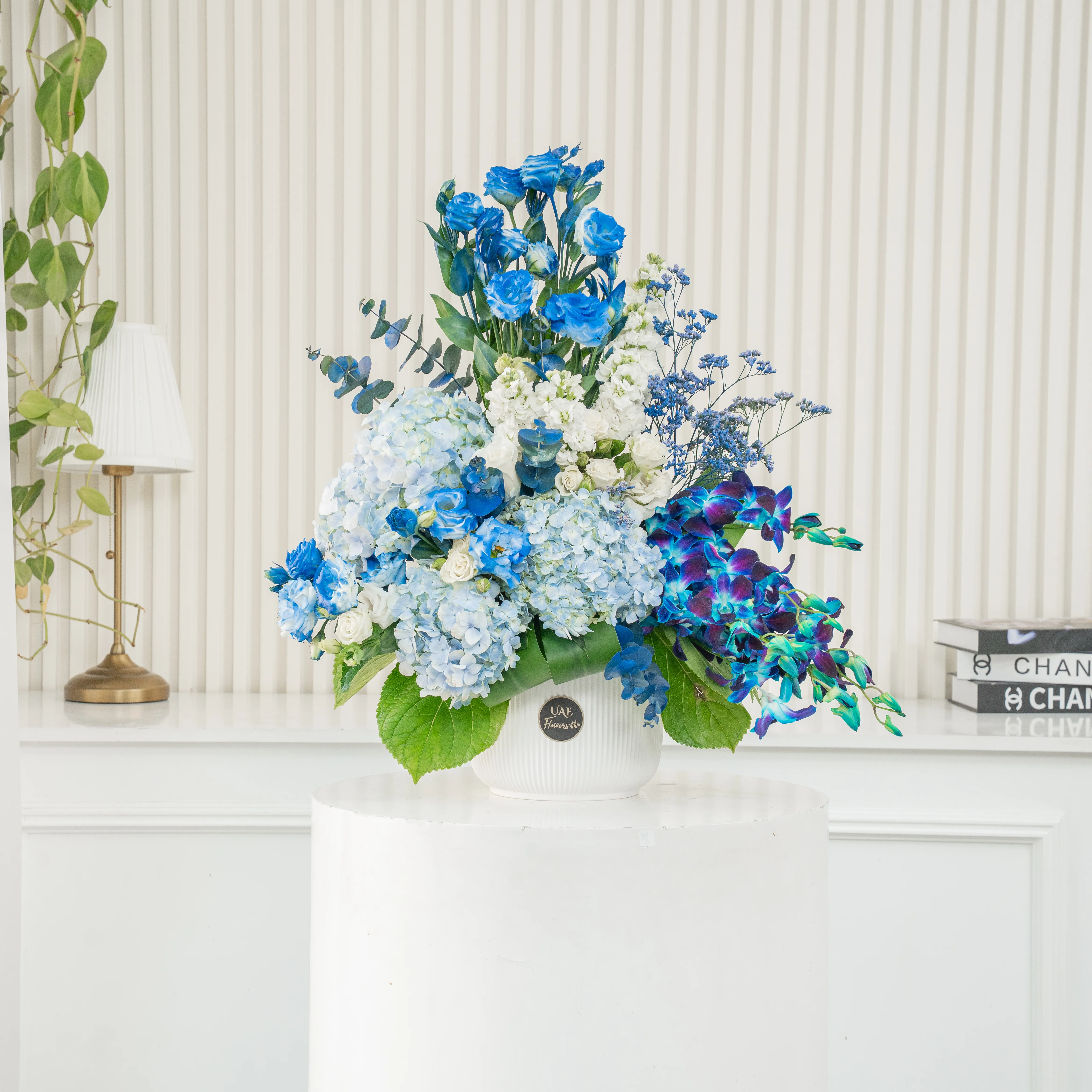 An arrangement of 10 white lisinathus, 5 white matthiola, 10 blue orchids, 5 white roses, 10 white spray roses and 3 blue hydrangeas with eucalyptus leaf and Limonium fillers in a ceramic pot.