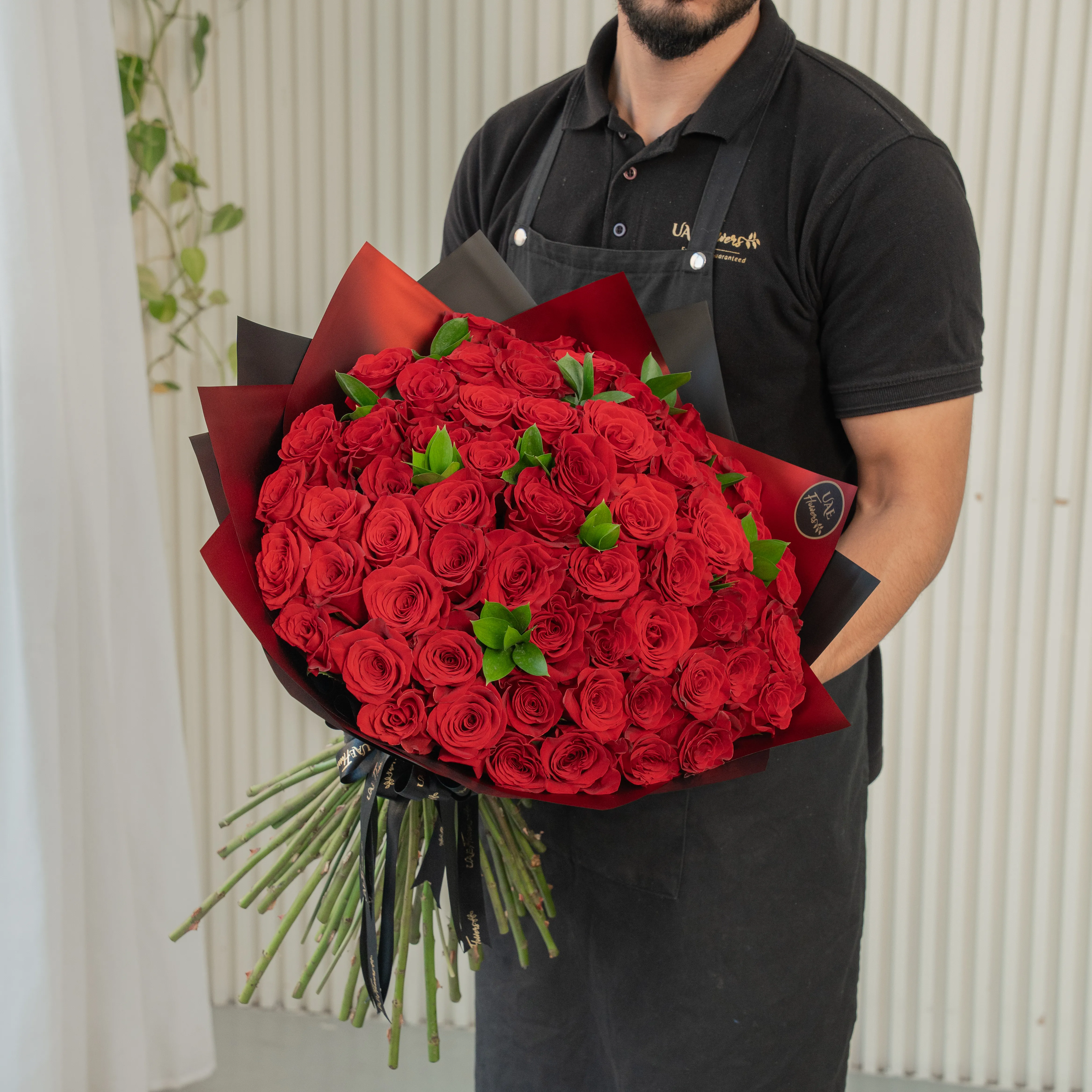 Bouquet of 100 red roses in paper packing hand-tied with ribbons.
